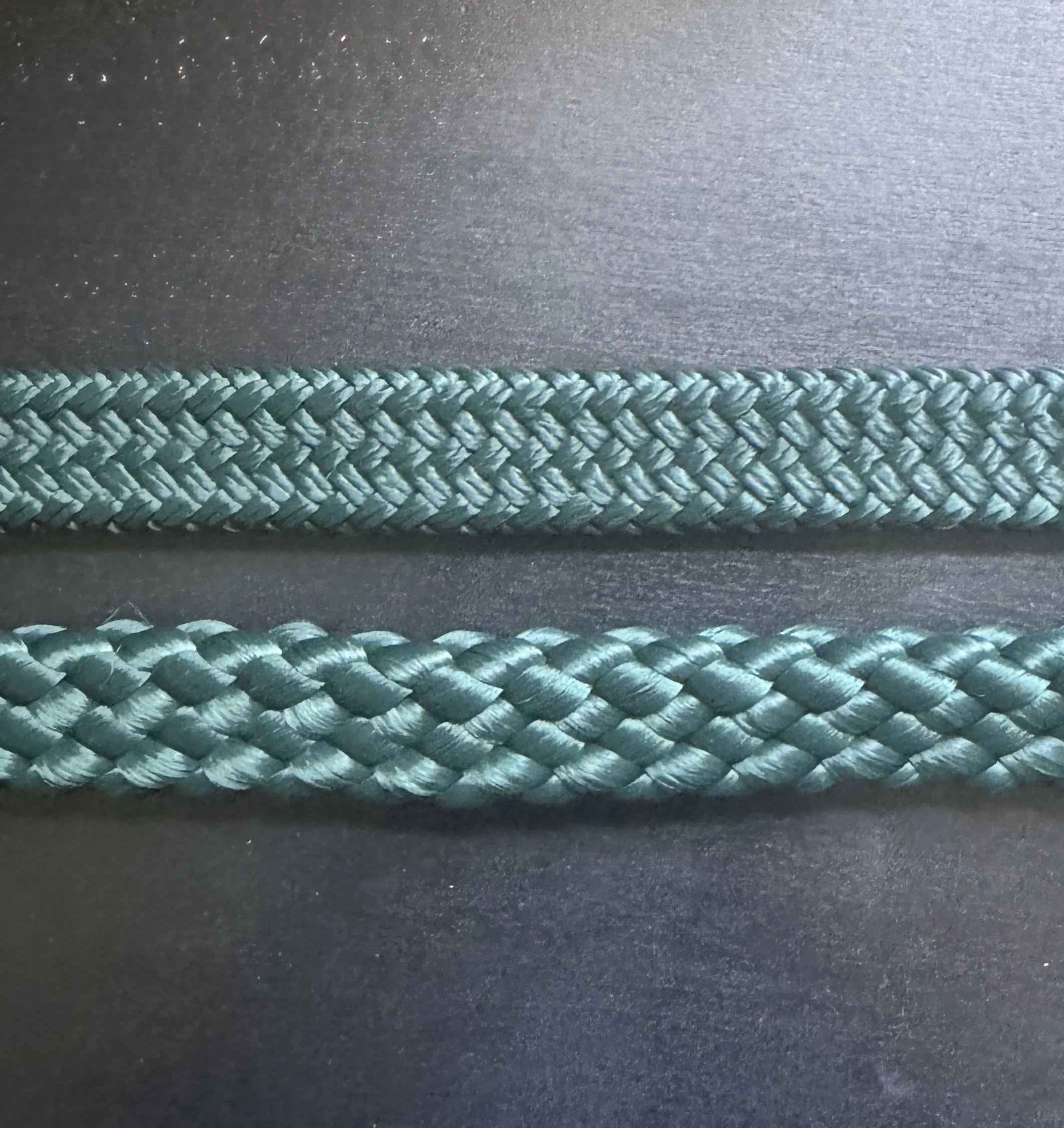Close-up of a braided teal rope on a black background. The top rope is tightly woven and thinner; the bottom rope is thicker.
