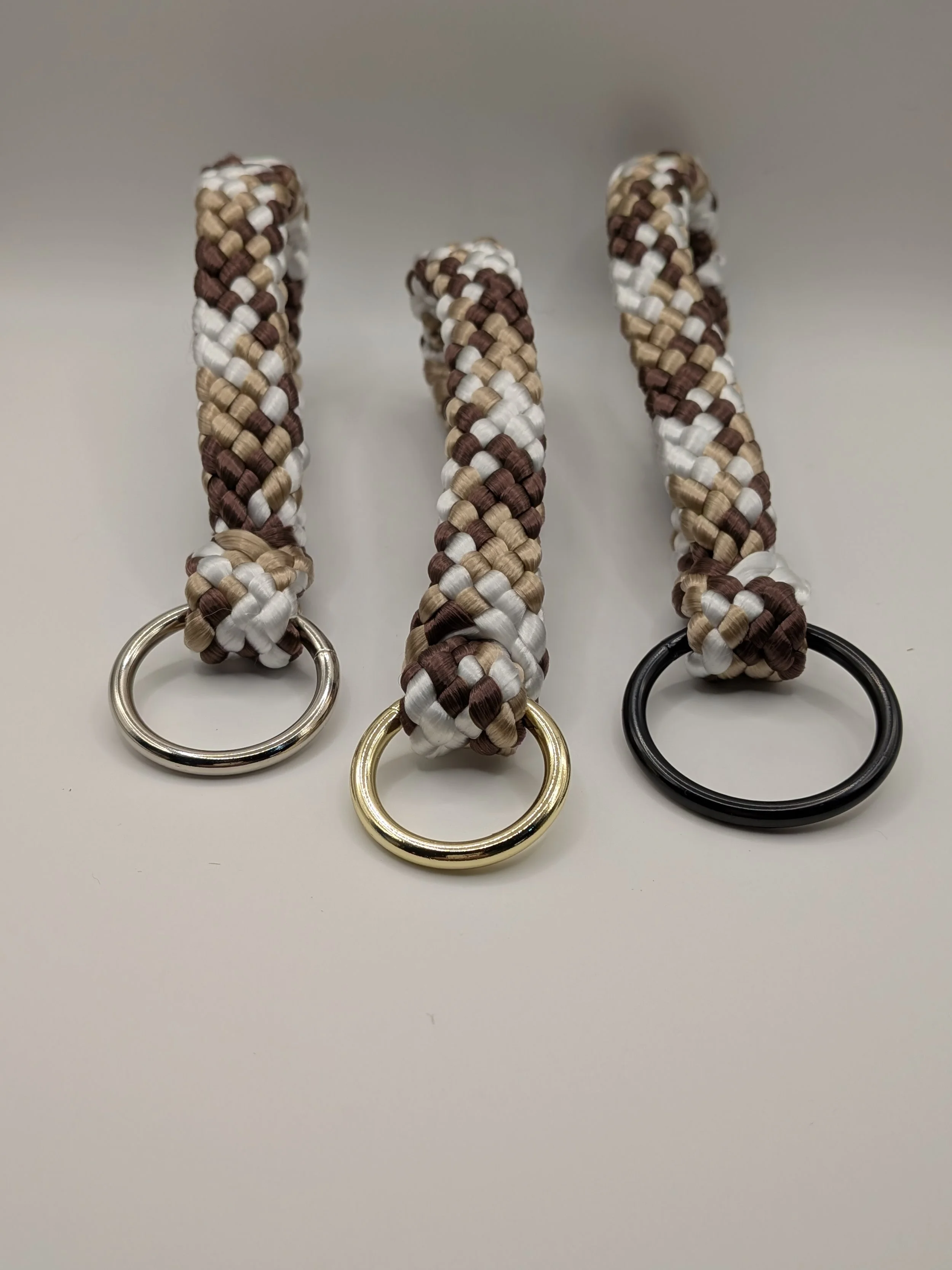 Three woven lanyards with metal rings at the end, each in different colors: silver, gold, and black.