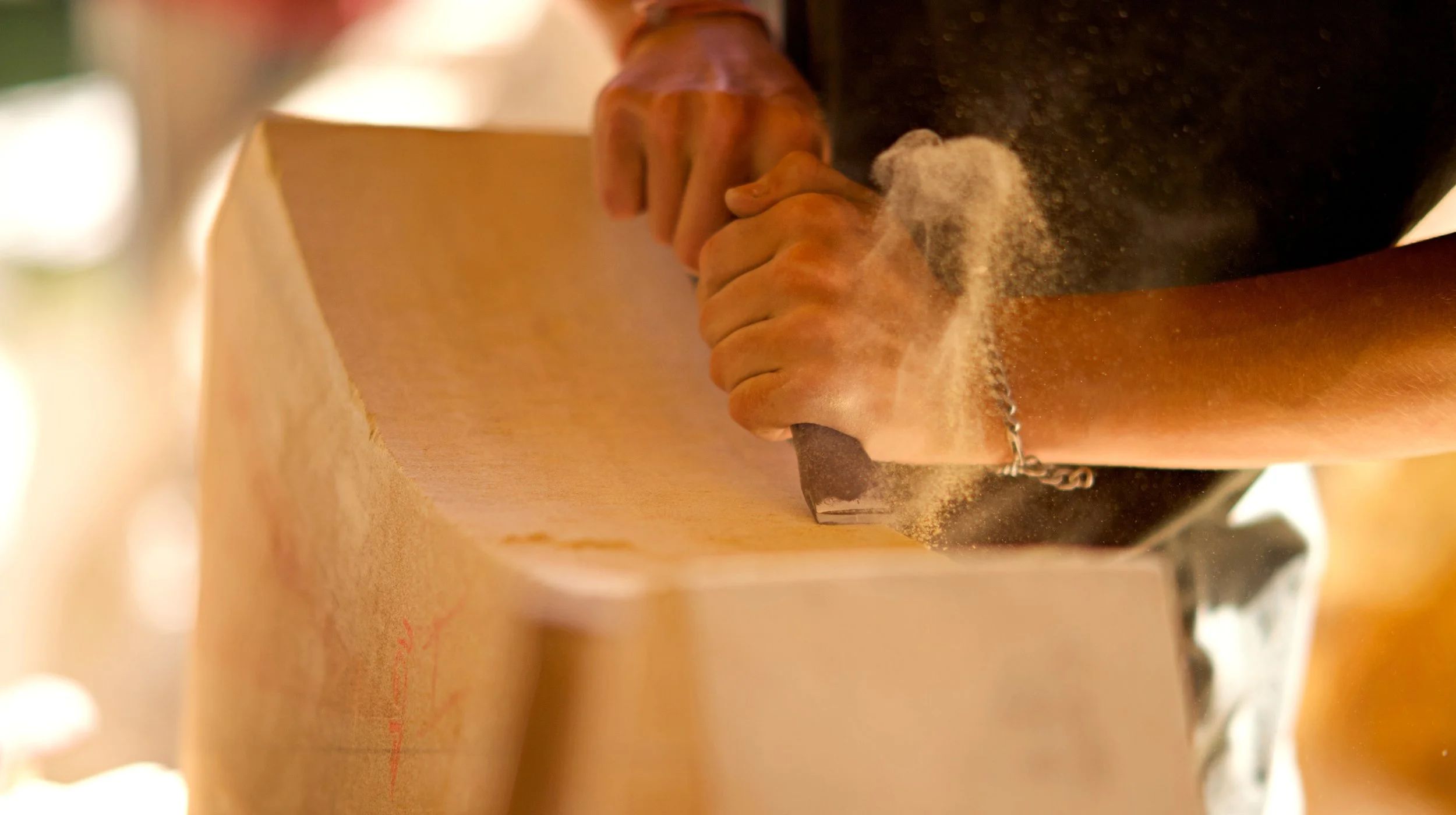 Personne utilisant une scie pour couper du bois dans un atelier, poussière de bois en suspension dans l'air.