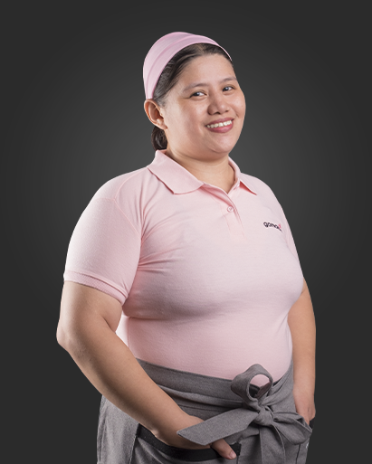 Woman in pink uniform with matching headscarf, standing and smiling against a dark background.