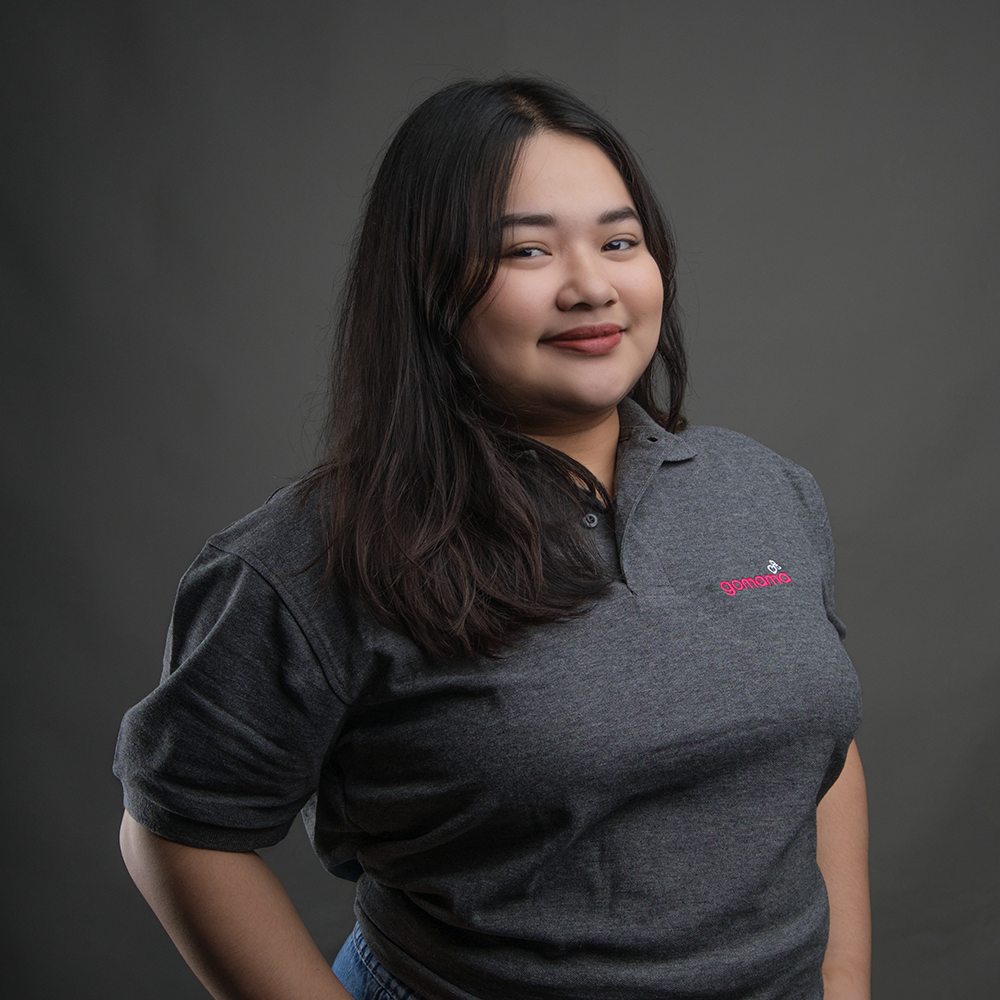 A young woman with long dark hair smiling, wearing a gray polo shirt with a pink logo, posing against a gray background.