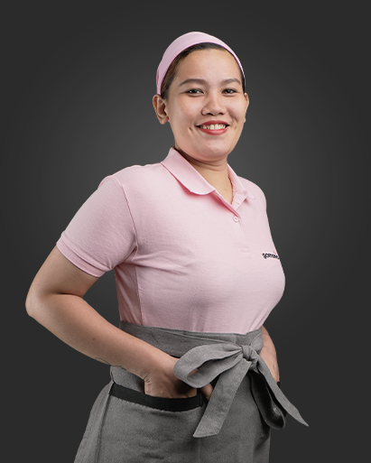 A woman with a pink uniform and headband smiling, standing with her hands on her hips against a dark background.