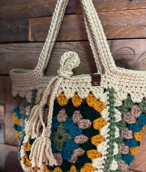 A multicolored crochet tote bag with a floral pattern, hanging on a wooden wall.