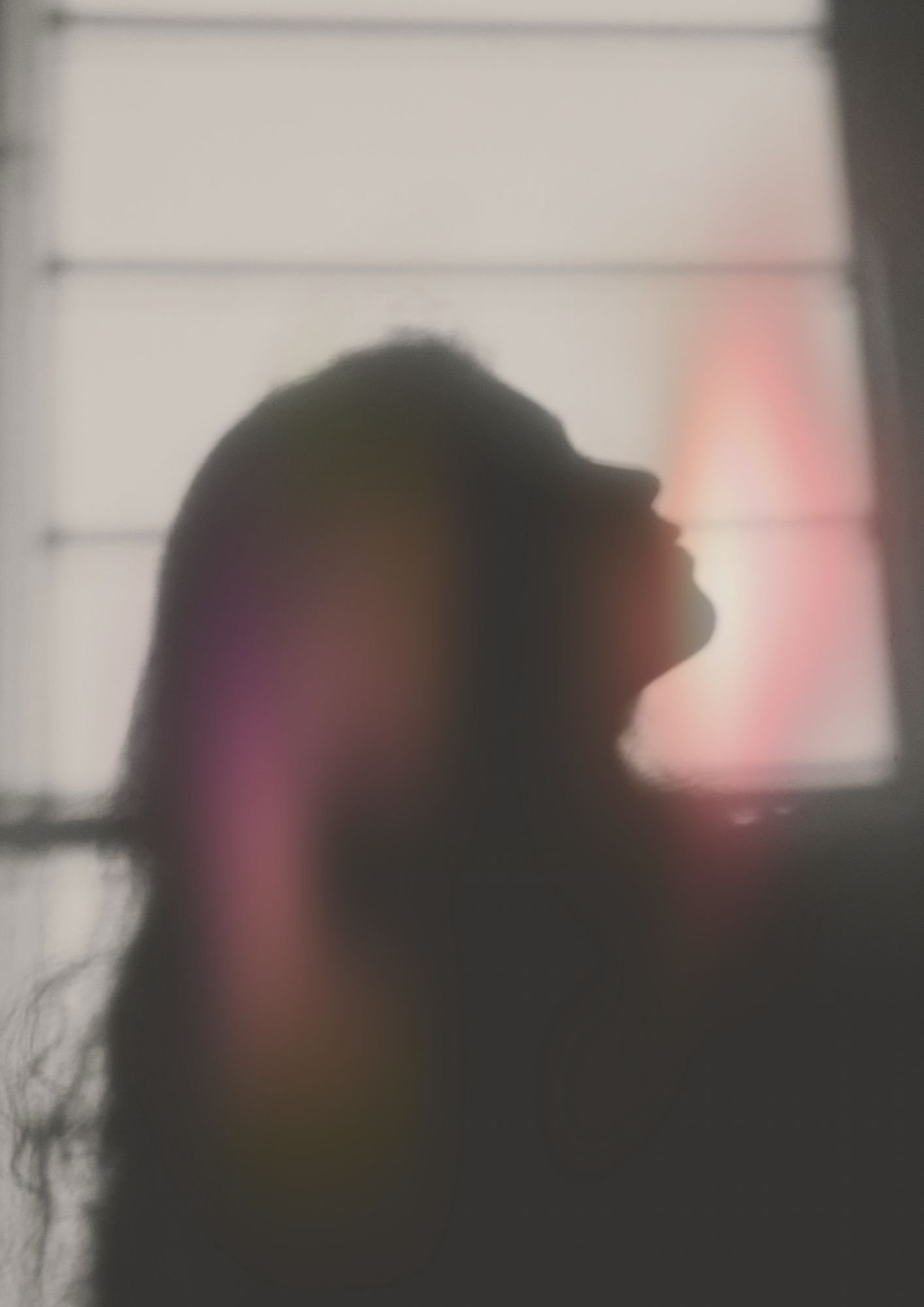 A blurry silhouette of a person's head in profile against a backlit background with grid lines or window panes.