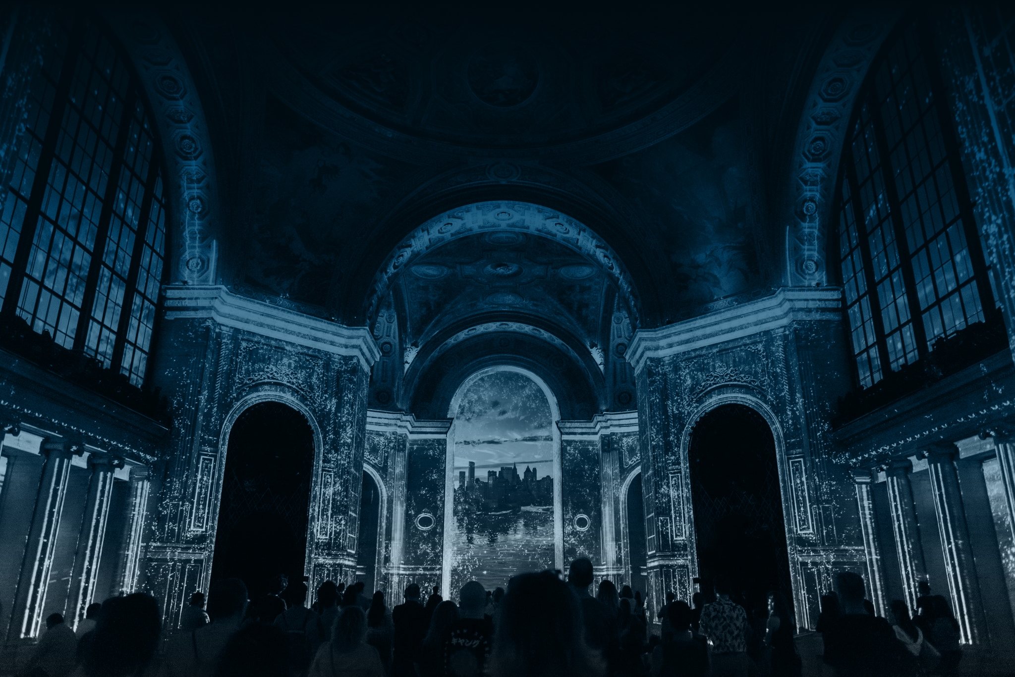People standing in front of a large projection of the moon and a city skyline on a grand architectural interior with arches and ornate details.