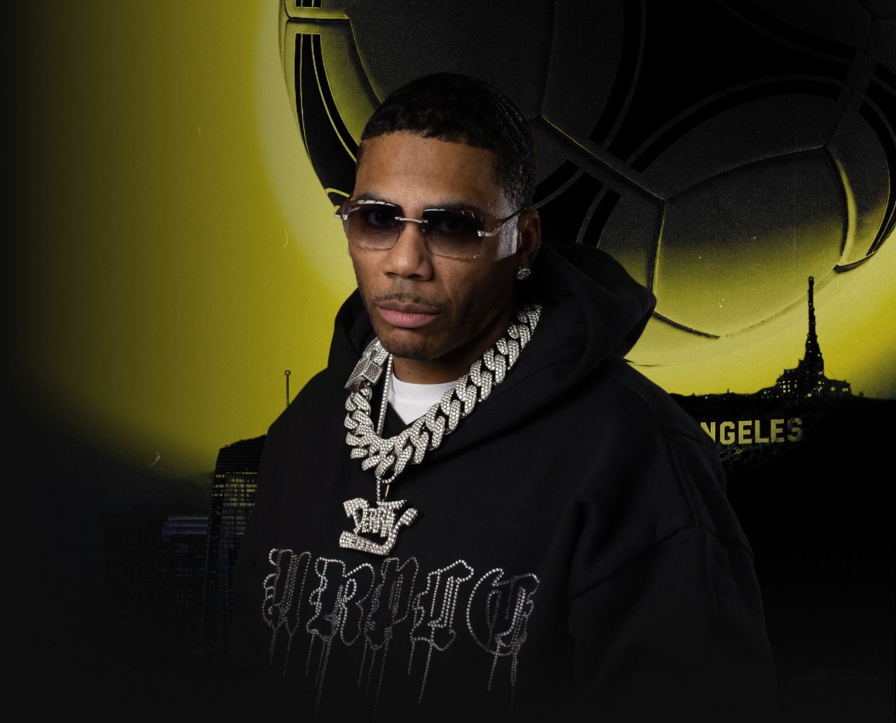 Man wearing sunglasses, diamond jewelry, and a black hoodie with text, standing in front of a Los Angeles-themed backdrop with a large yellow moon and a spaceship.