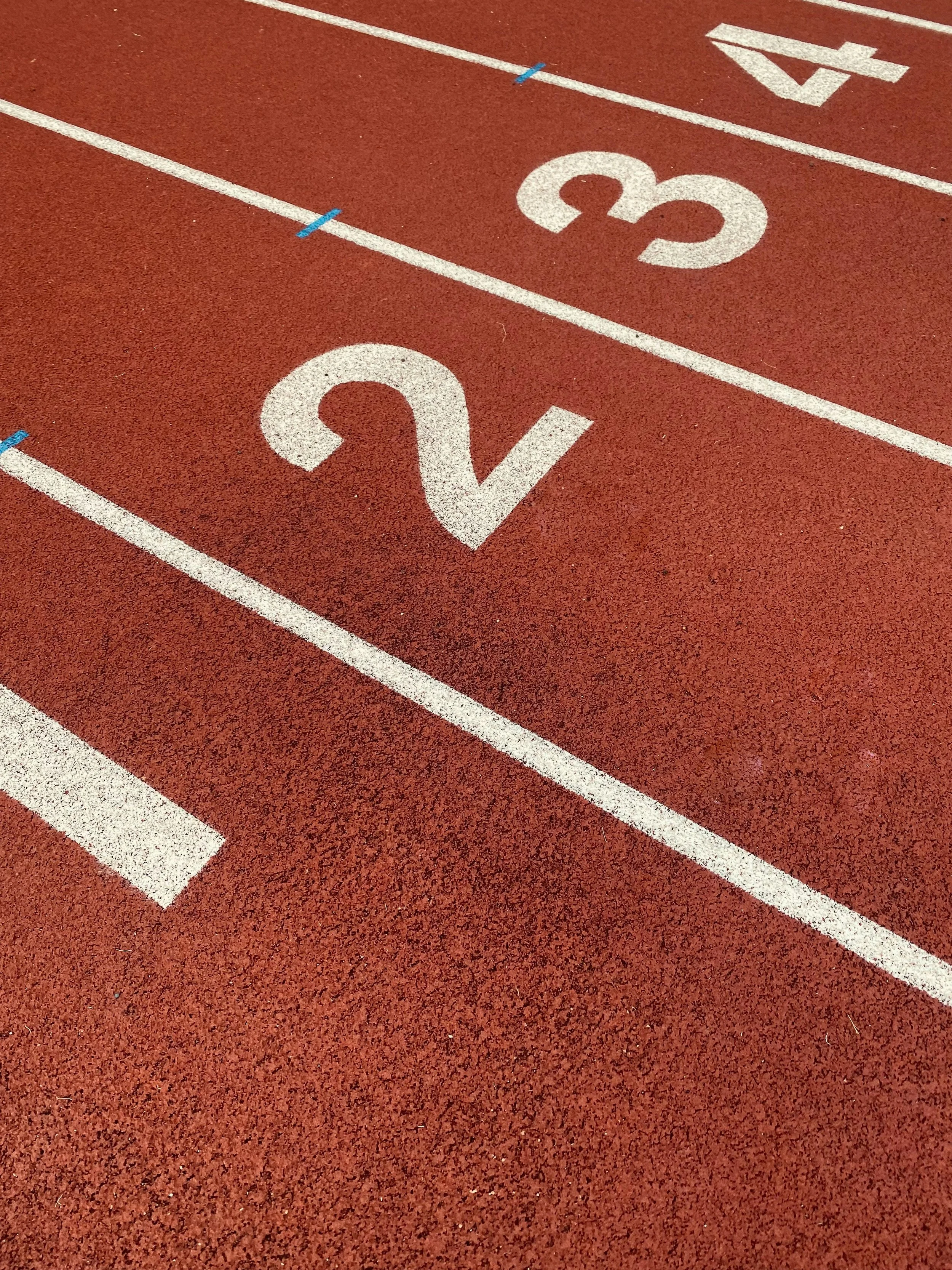 A red running track with white lane numbers 2, 3, and 4 visible, and blue lane markers.