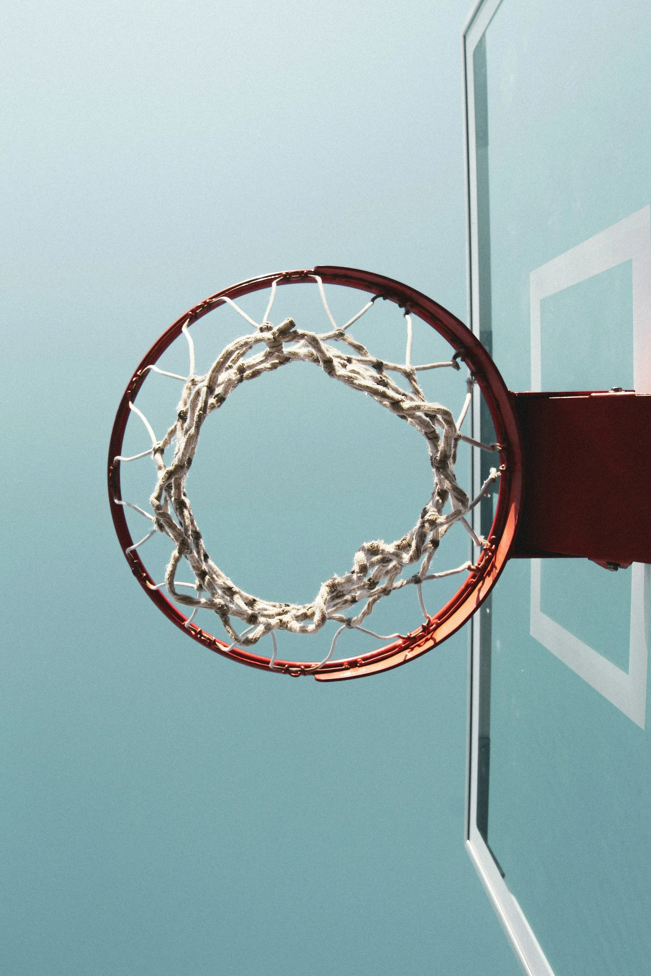 A basketball hoop with a net hangs from a backboard on a clear blue sky.