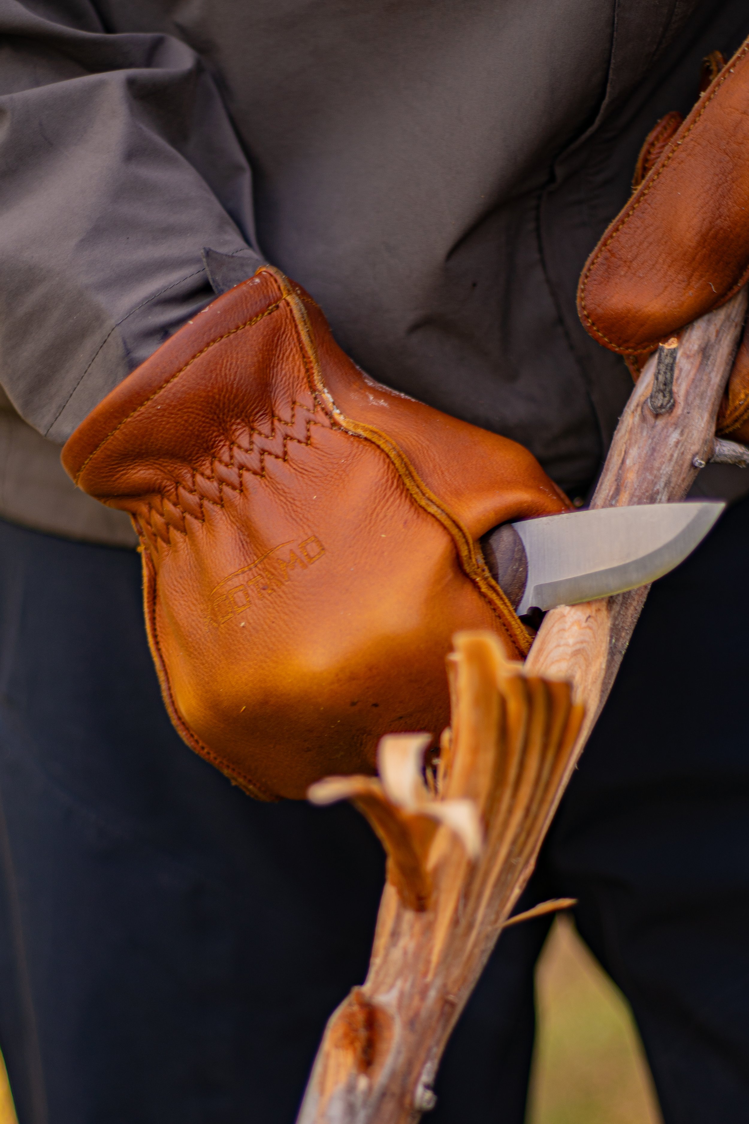Close-up of a person wearing a gray jacket and brown leather gloves, holding a long wooden stick or branch.