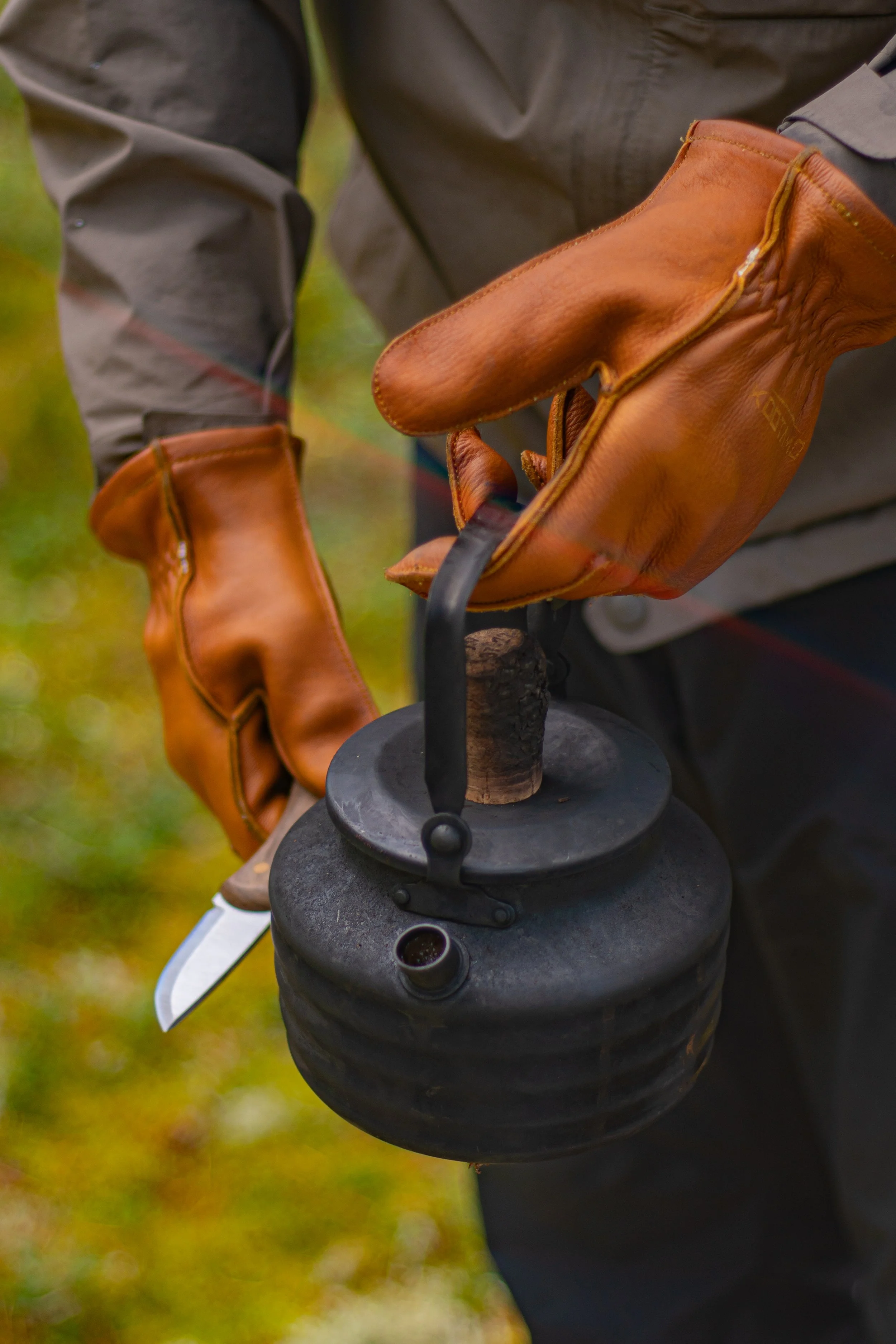 Close-up of a person holding a pair of vintage leather gloves, with a black lantern and an outdoor background.