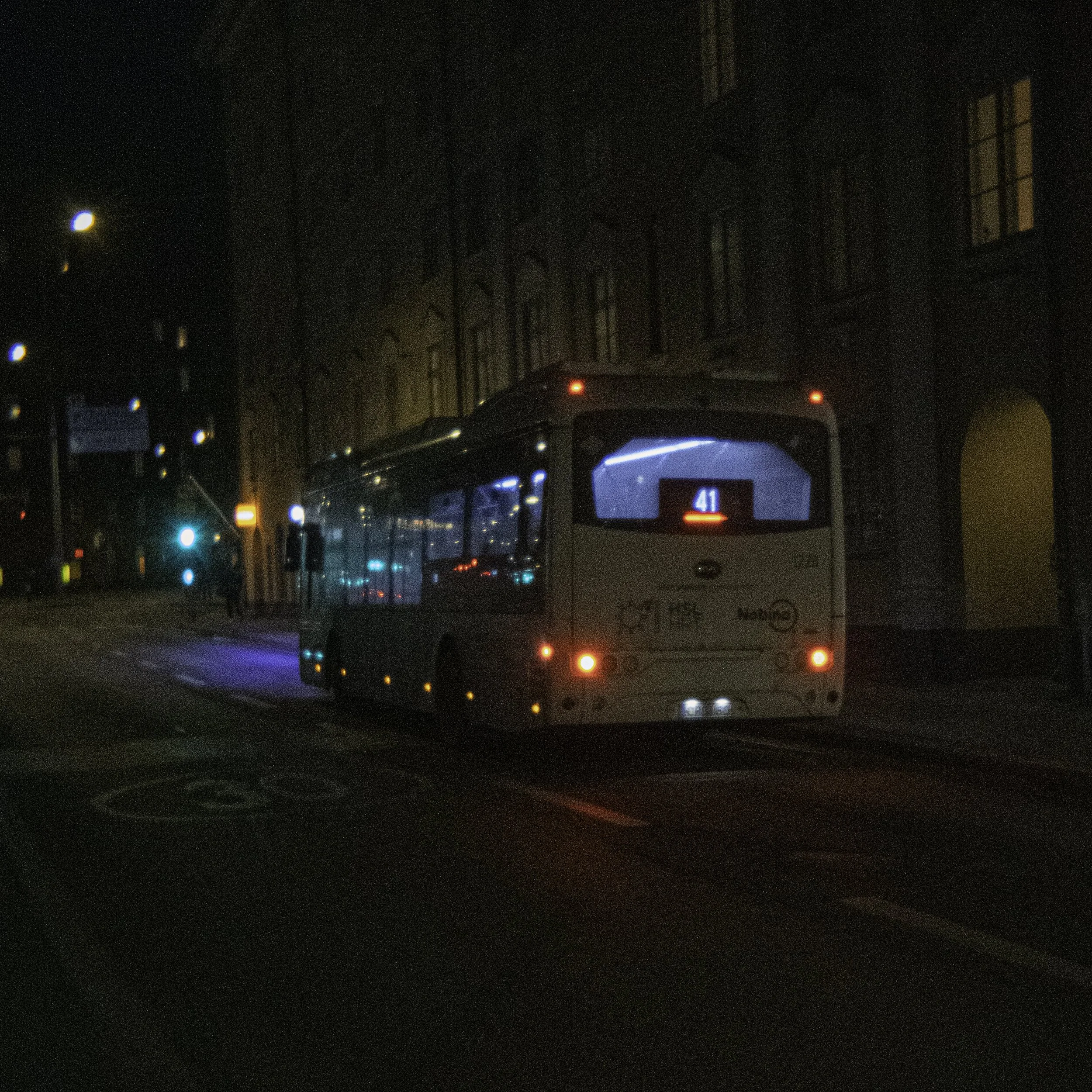 Nighttime street scene with cars stopped at a traffic light and buildings with lit windows in the background.