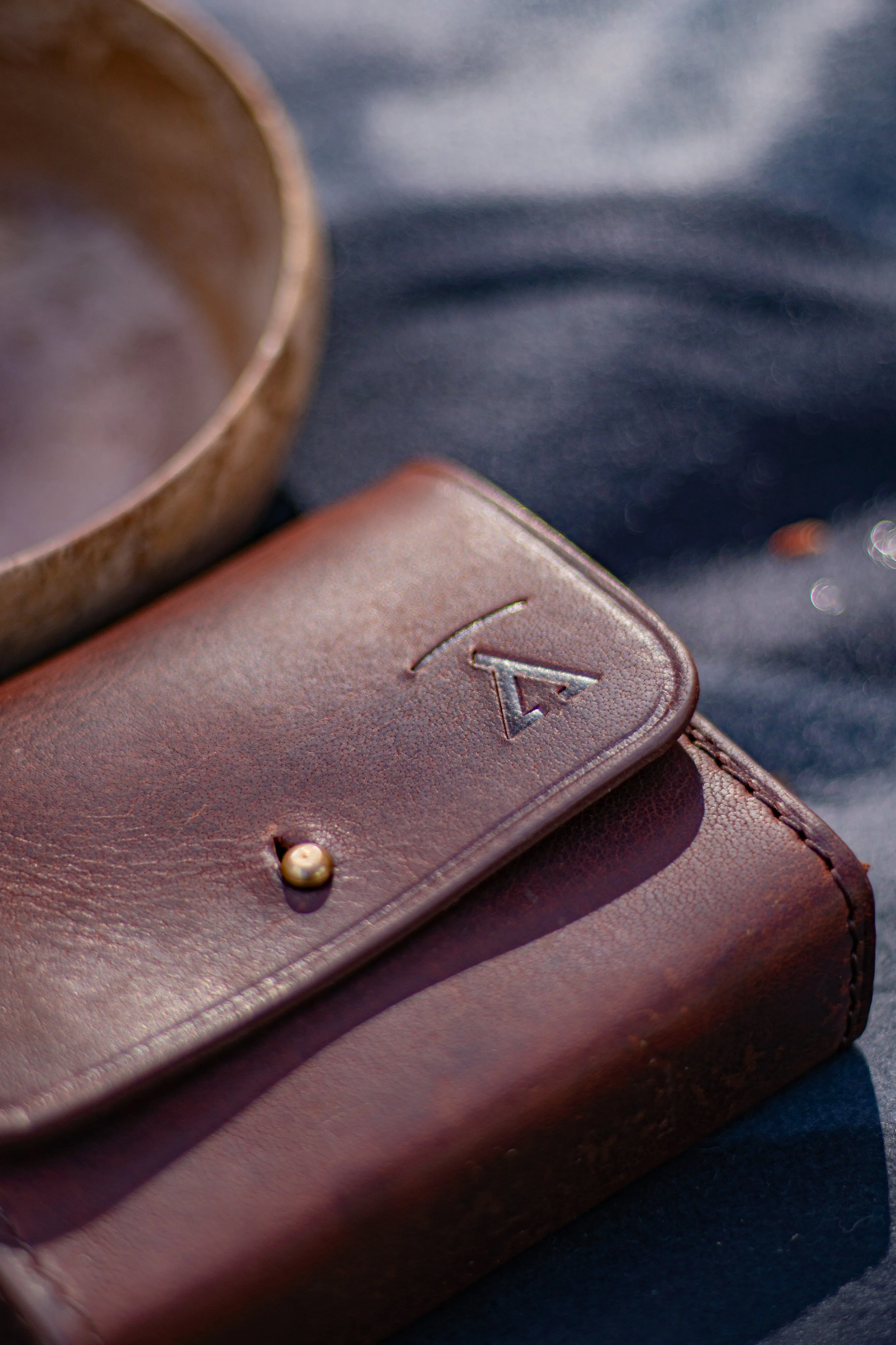 Close-up of a brown leather LG phone case with a small letter 'A' embossed on the flap, placed on dark fabric.