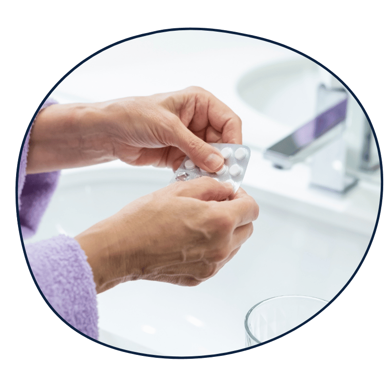 Close-up of a person holding a blister pack of white pills over a bathroom sink.