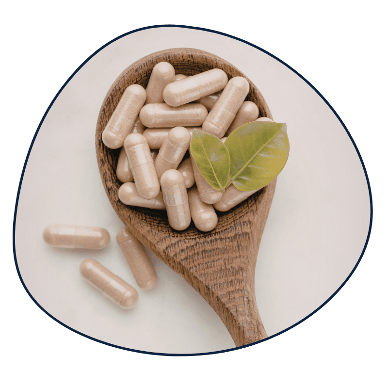 Wooden spoon filled with beige supplement capsules, topped with green leaves, on a white surface.