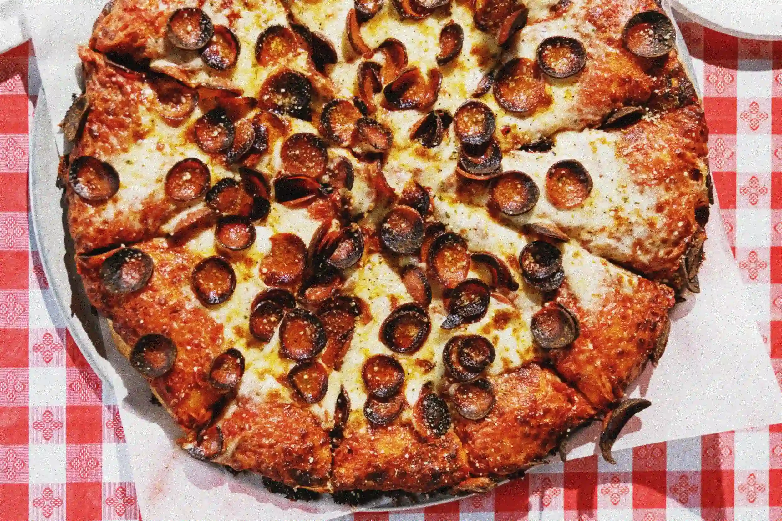 Heart-shaped pizza topped with pepperoni slices and black olives, sitting on a red and white checkered paper.