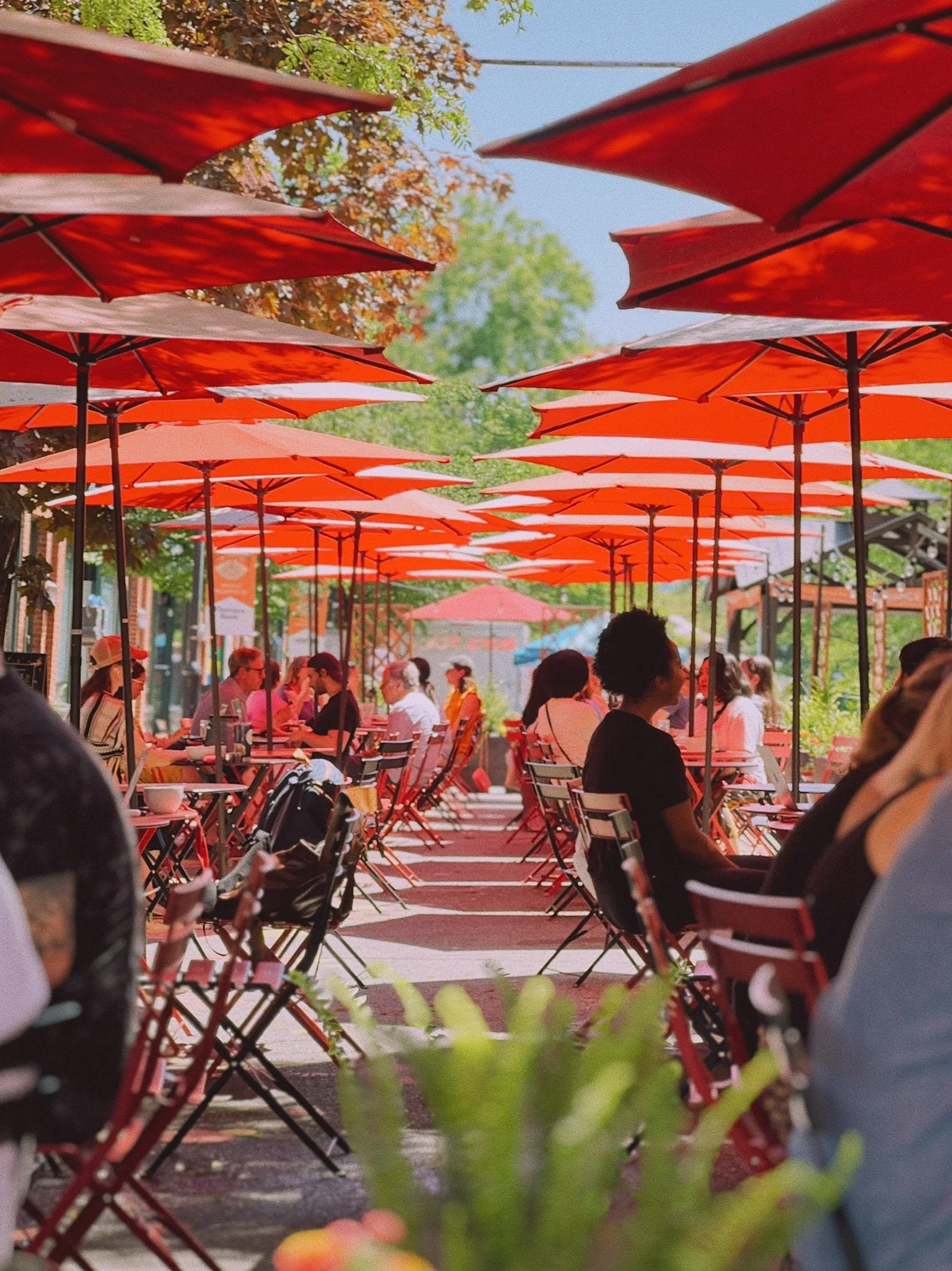 Dining at tables with red umbrellas on Strong Ave, during Summer on Strong