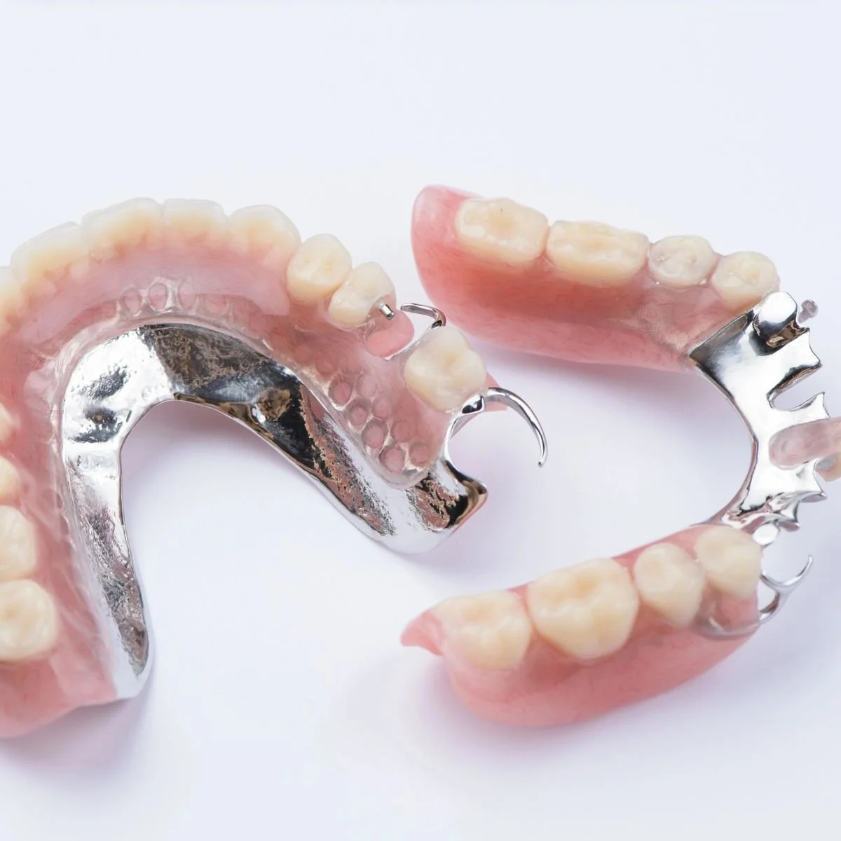A set of partial dentures with artificial teeth and metal framework, resting on a white surface.
