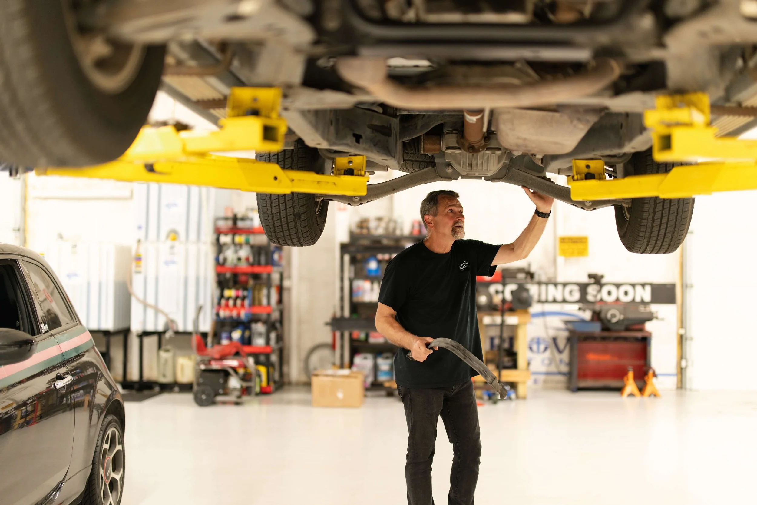 A mechanic inspecting the underside of a vehicle on a lift in a well-lit garage, with tools and equipment in the background.