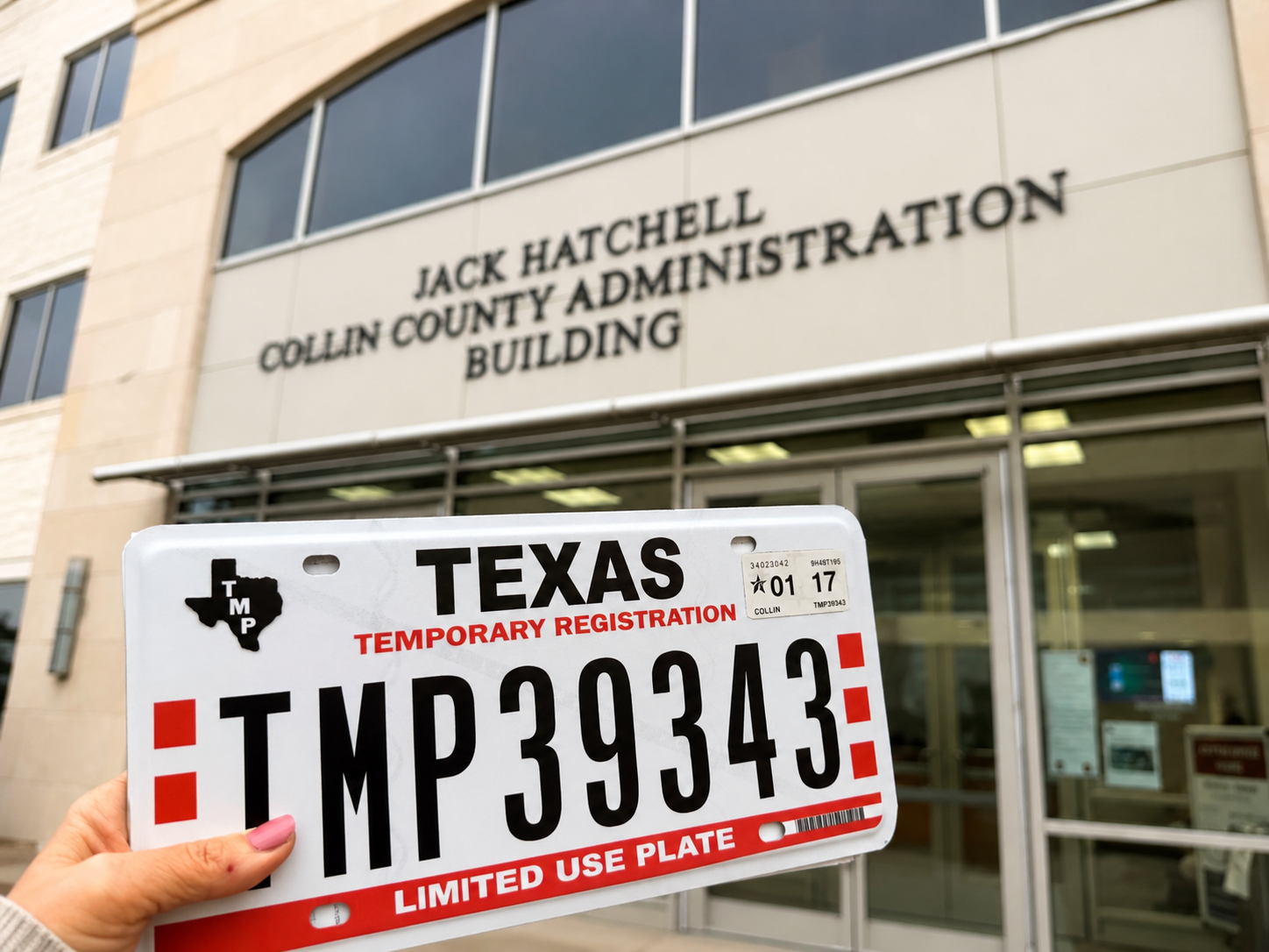 A person holding a Texas temporary vehicle registration plate outside the Jack Hatchett Collin County Administration Building.