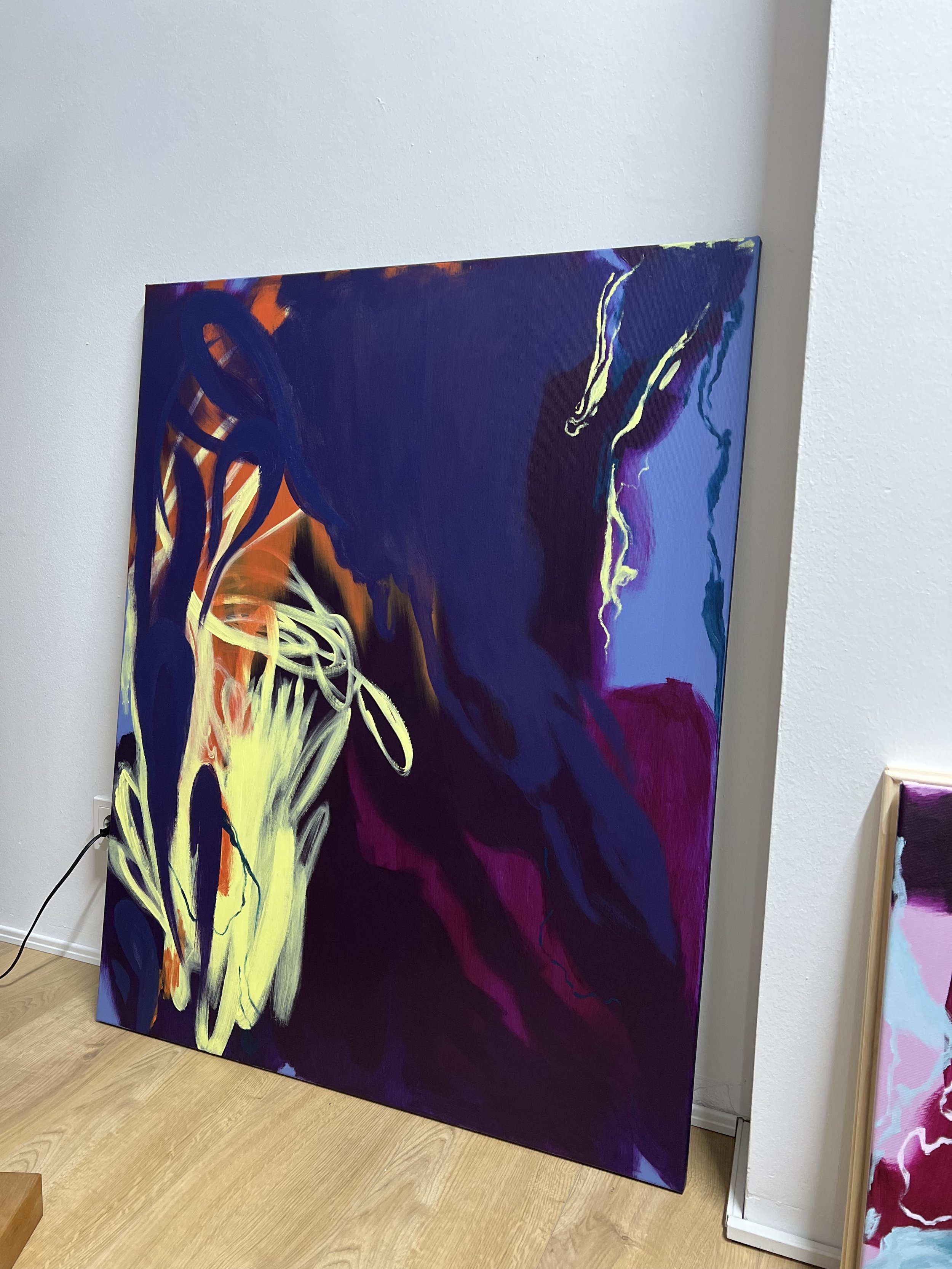 An abstract colorful painting with bold strokes of purple, yellow, orange, black, blue, and pink, displayed on an easel in an art gallery.