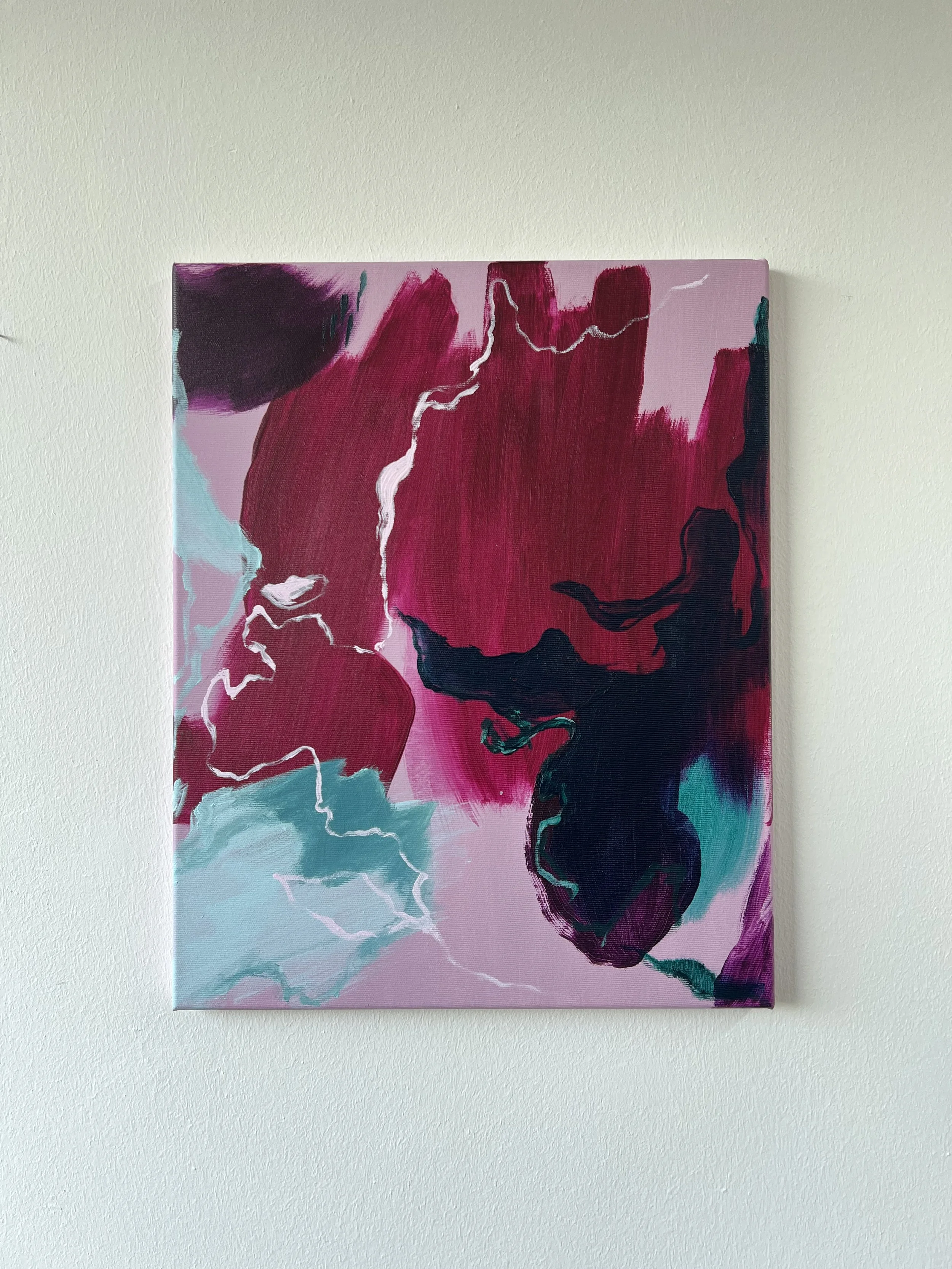 Abstract painting with shades of pink, black, teal, and white, featuring bold brush strokes and a white lightning-like line, mounted on a plain white wall.