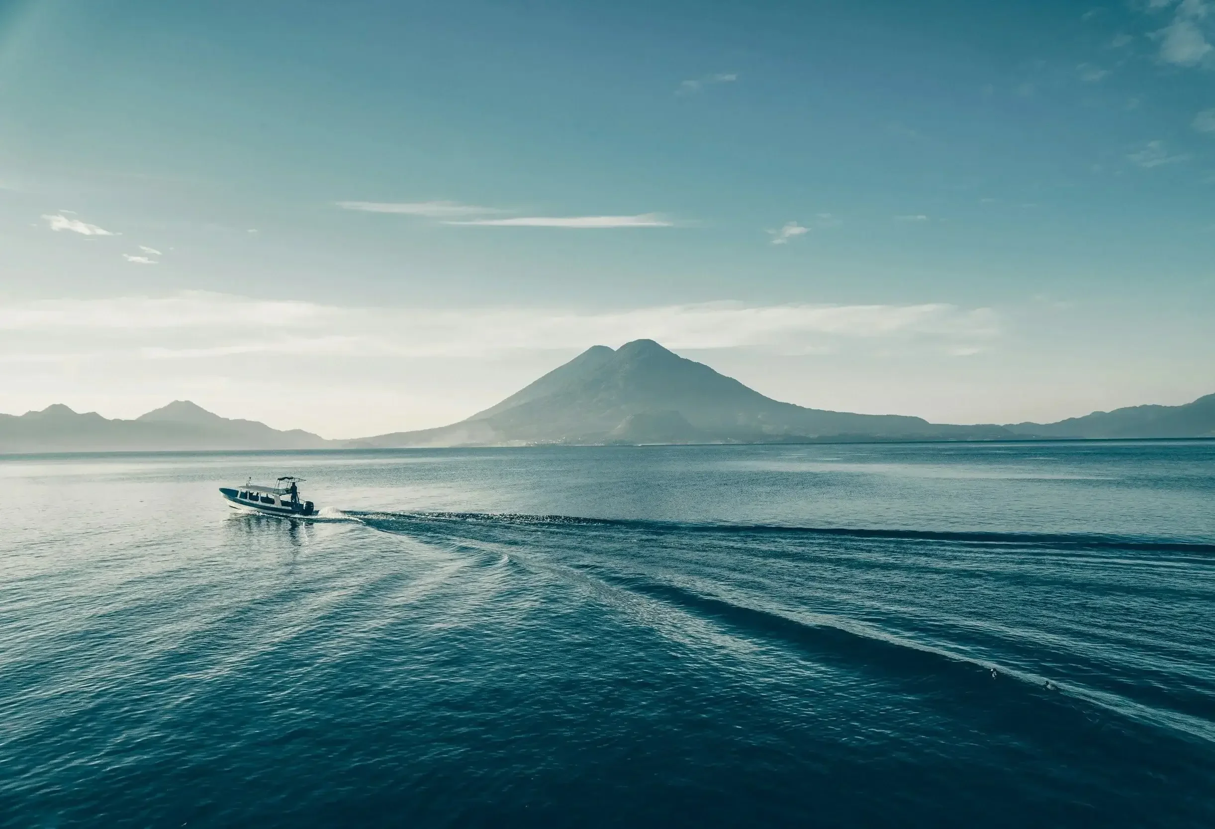 A small boat moving across the ocean with a mountain in the background under a mostly clear sky.