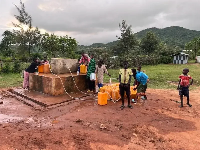 People collecting water using containers at a water well in a rural area.