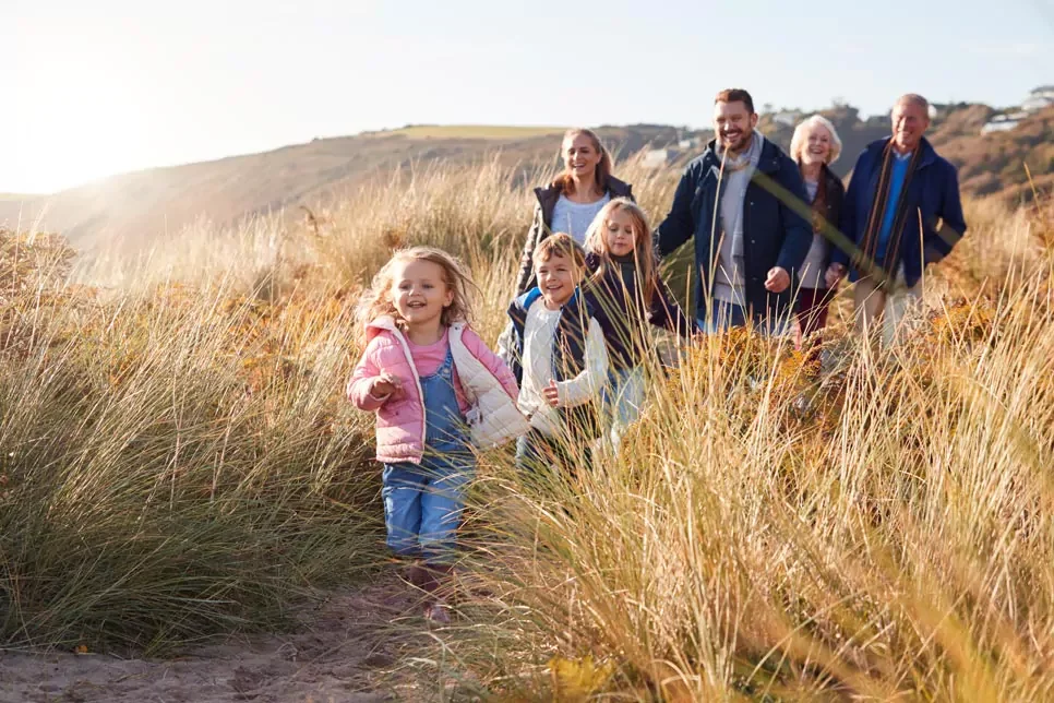 A family of seven, including three children and four adults, walking through tall grass on a hillside during sunset.