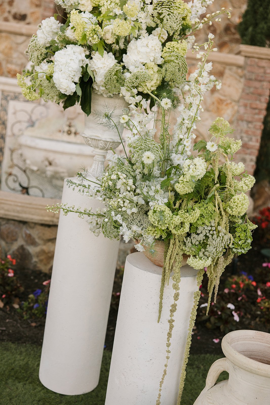 White and green floral arrangements on white cylindrical pedestals in an outdoor setting.