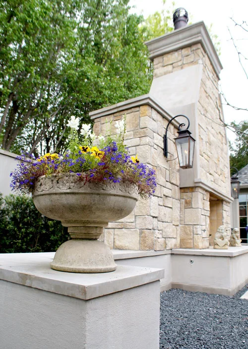 Left: Season color in a concrete planter rests atop pedestals on either side of the outdoor fireplace.