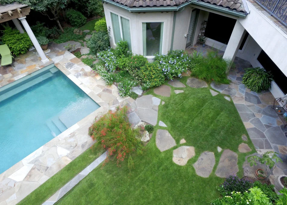 The use of circles and ellipses in this space give a bold, expressive sense of unity that cohesively connects the pool, house, and raised deck, creating a sense of oneness throughout. Flagstone was used to deconstruct the sharp edge of the pool whic…