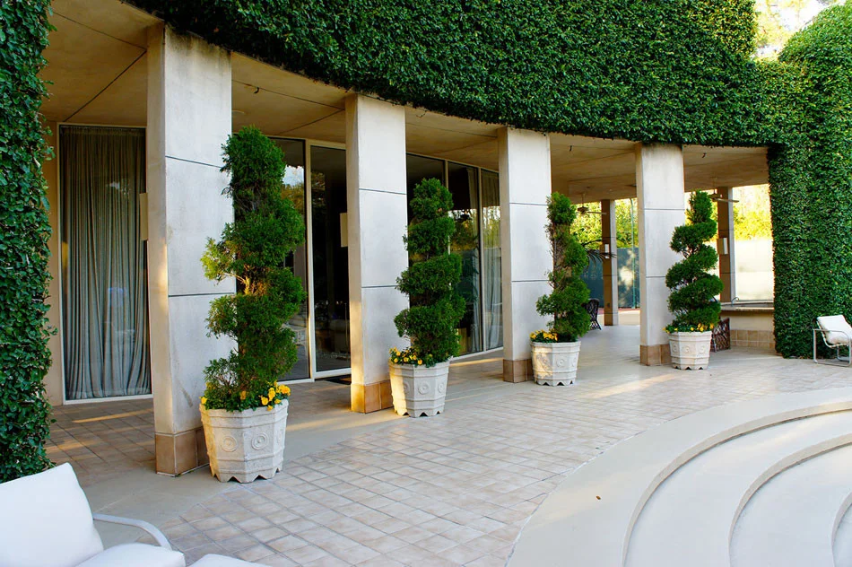 Container grown Italian cypress and spiral juniper add interesting visual elements and a grand, ivy-covered wall give the space a geometric, art deco appeal.
