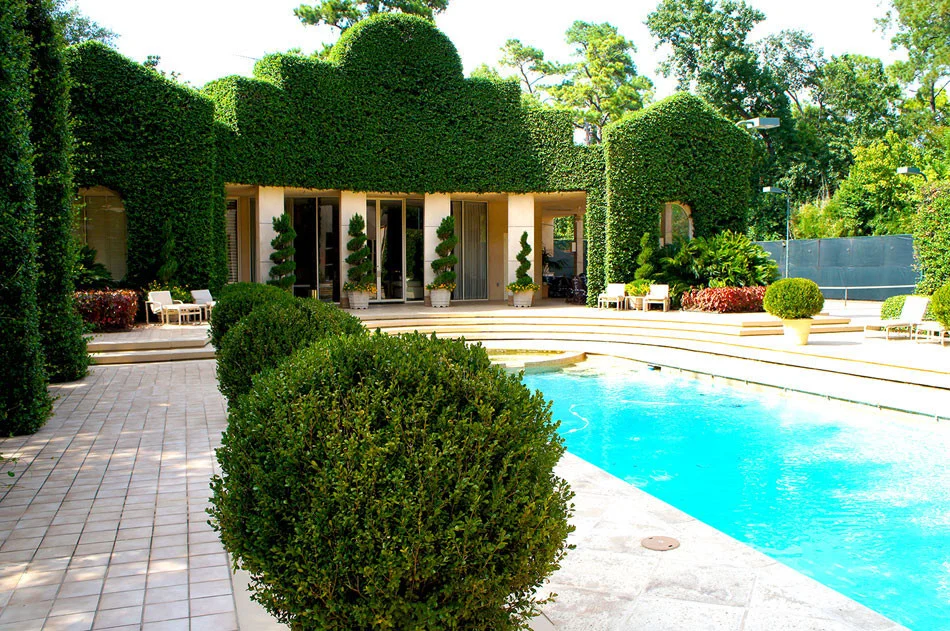 The backyard boasts an ornate, poolside retreat. Container grown Italian cypress and spiral juniper add interesting visual elements and a grand, ivy-covered wall give the space a geometric, art deco appeal. Ivy arches, carved columns, and sharply pr…