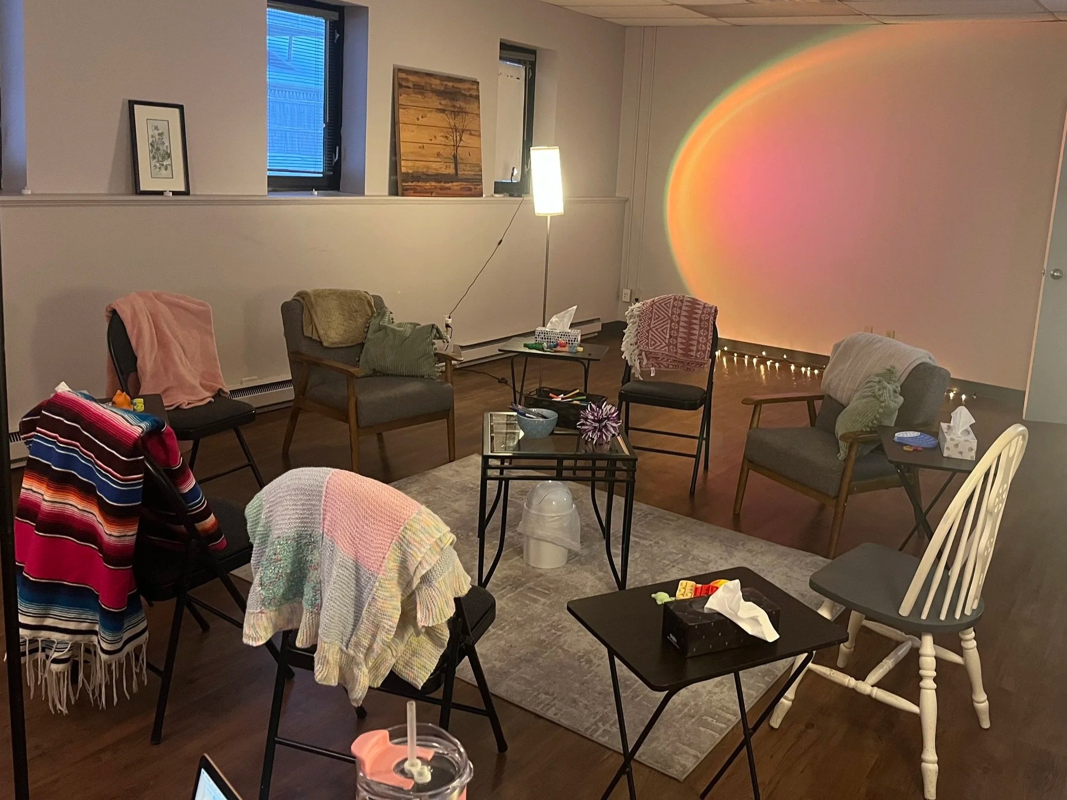 Living room with chairs, tables, artwork on the wall, and a colorful rainbow light projection on the wall.