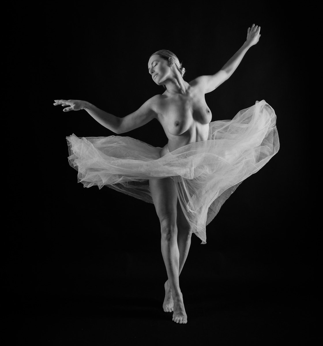 Monochrome fine-art photograph of a female dancer in motion, surrounded by flowing fabric against a black background.