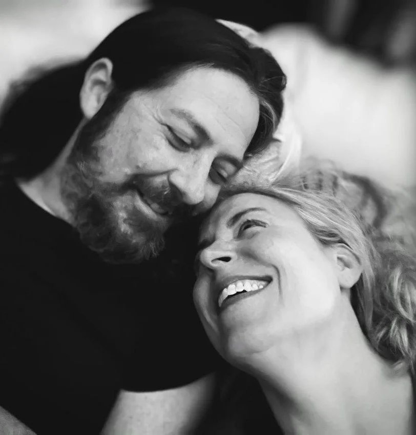 A black and white photo of a man and woman smiling and looking at each other affectionately, with their heads close together.