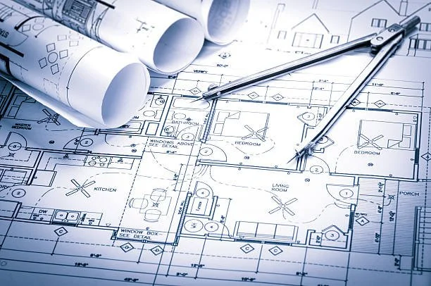 Blueprints of a house with rolled architectural plans and drawing tools.
