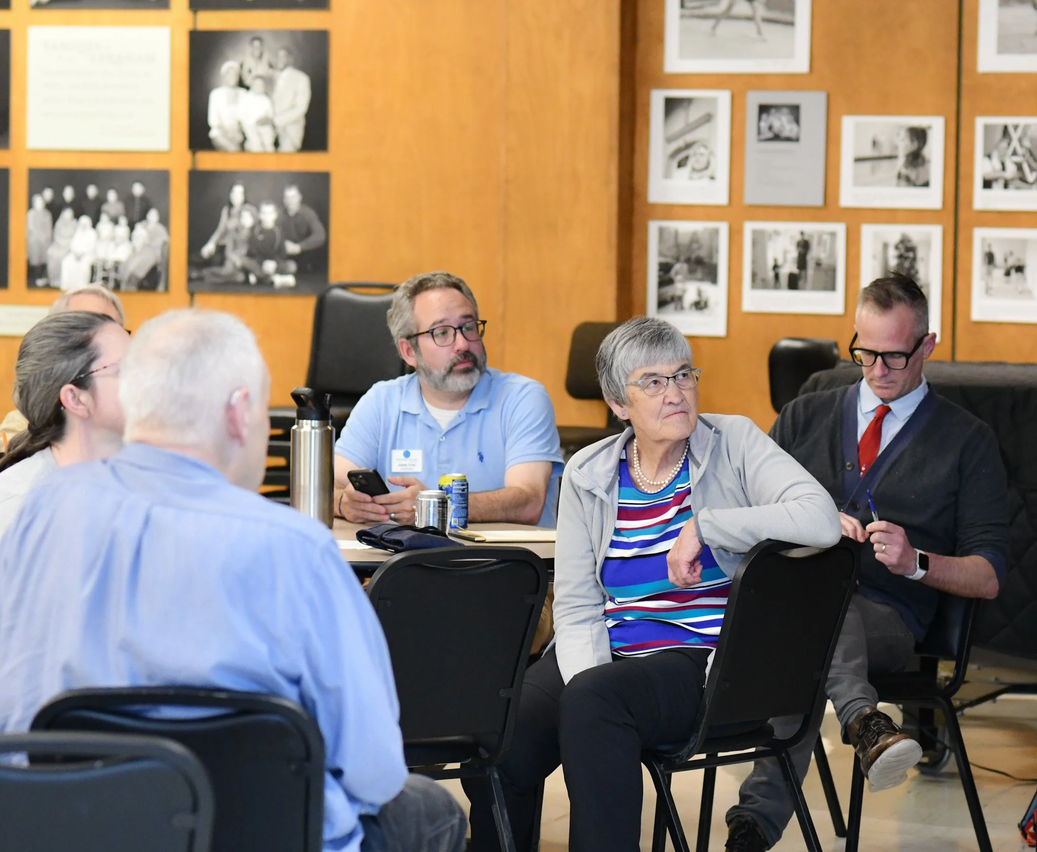 People sitting around a table in a meeting room with wood-paneled walls decorated with black and white photographs.