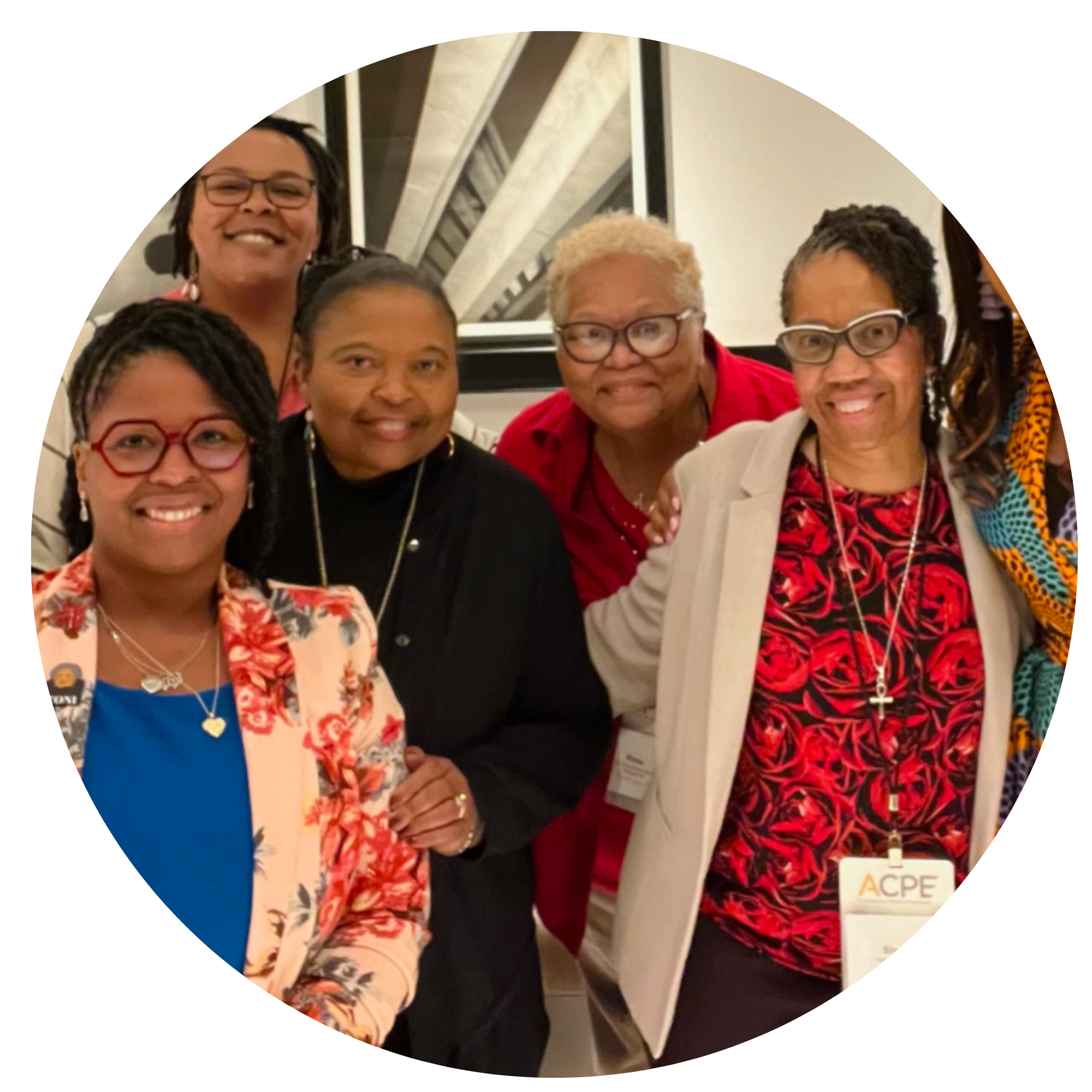 Group of diverse women smiling, posing together at an indoor event, some wearing glasses and colorful clothing, with an ACPE stand visible in the background.