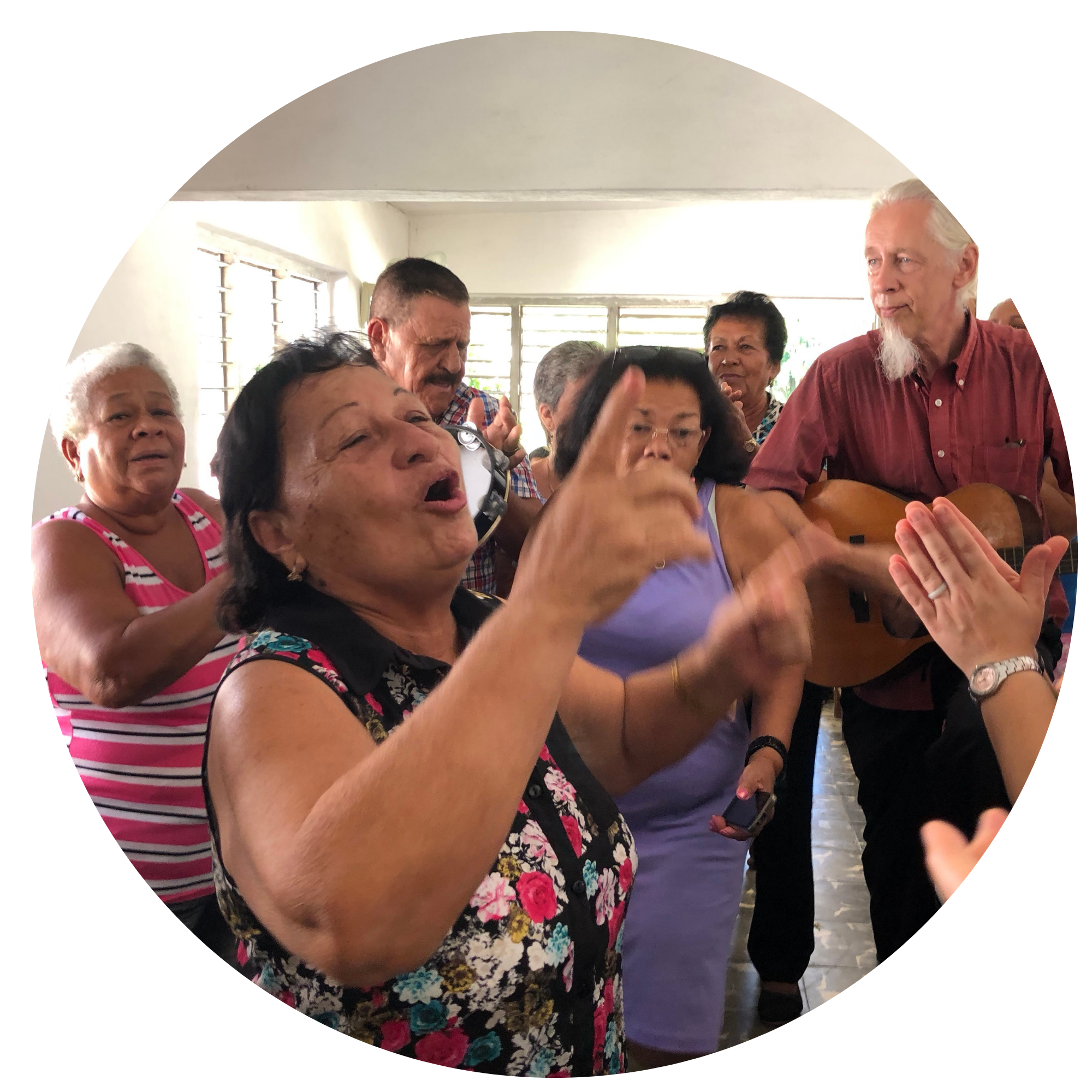 Group of elderly people smiling and singing together in a room, some holding musical instruments.