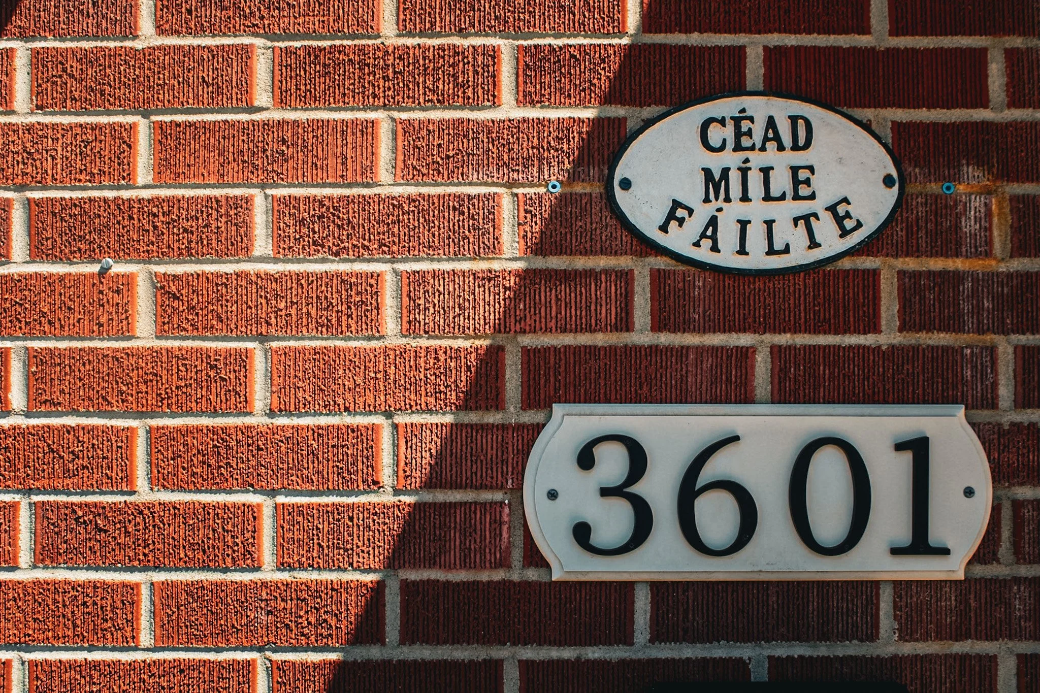 A brick wall with a house number plaque and a street sign reading "Cead Mile Fáilte".