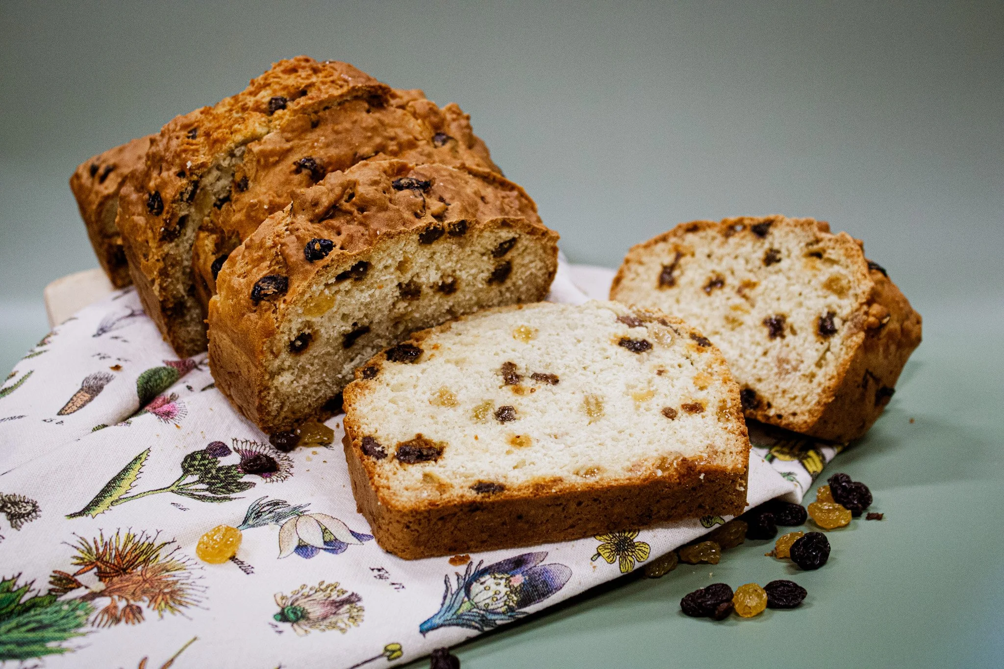 Two slices of raisin cake on a floral cloth with scattered raisins around.