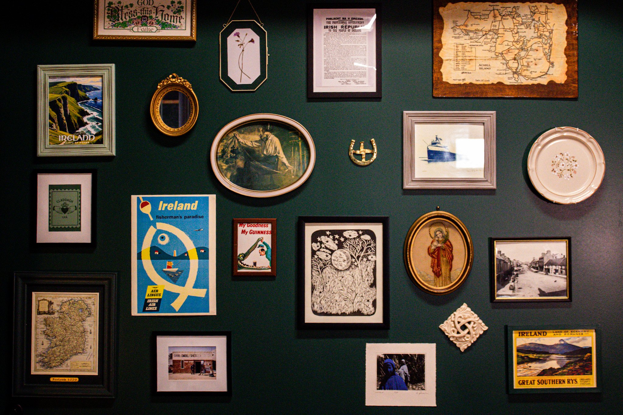 A wall decorated with various framed pictures and posters related to Ireland, including maps, artwork, and travel posters, arranged in a gallery style.