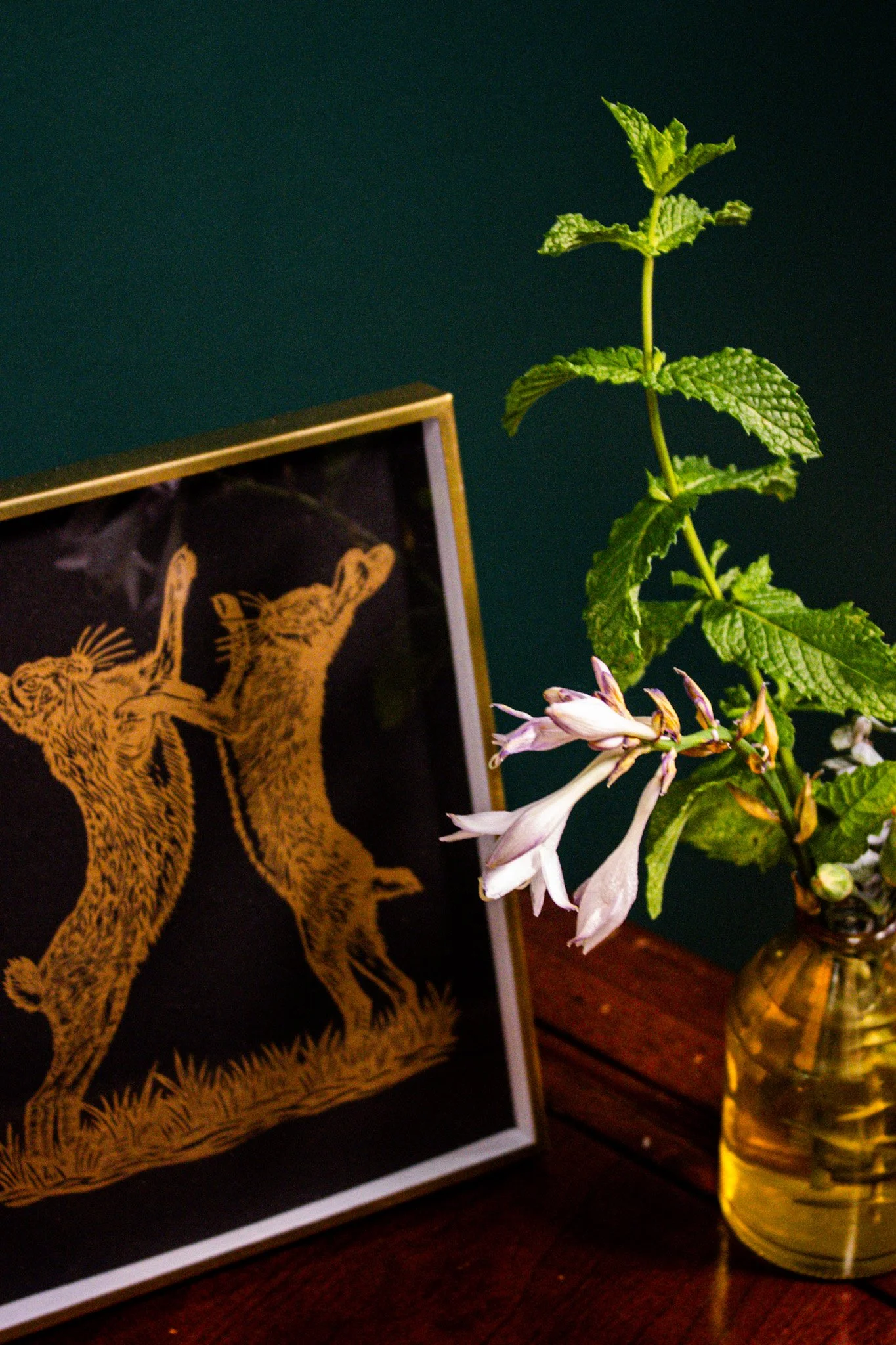 Close-up of a potted plant with white flowers and green textured leaves, positioned next to a framed artwork featuring two leopards.