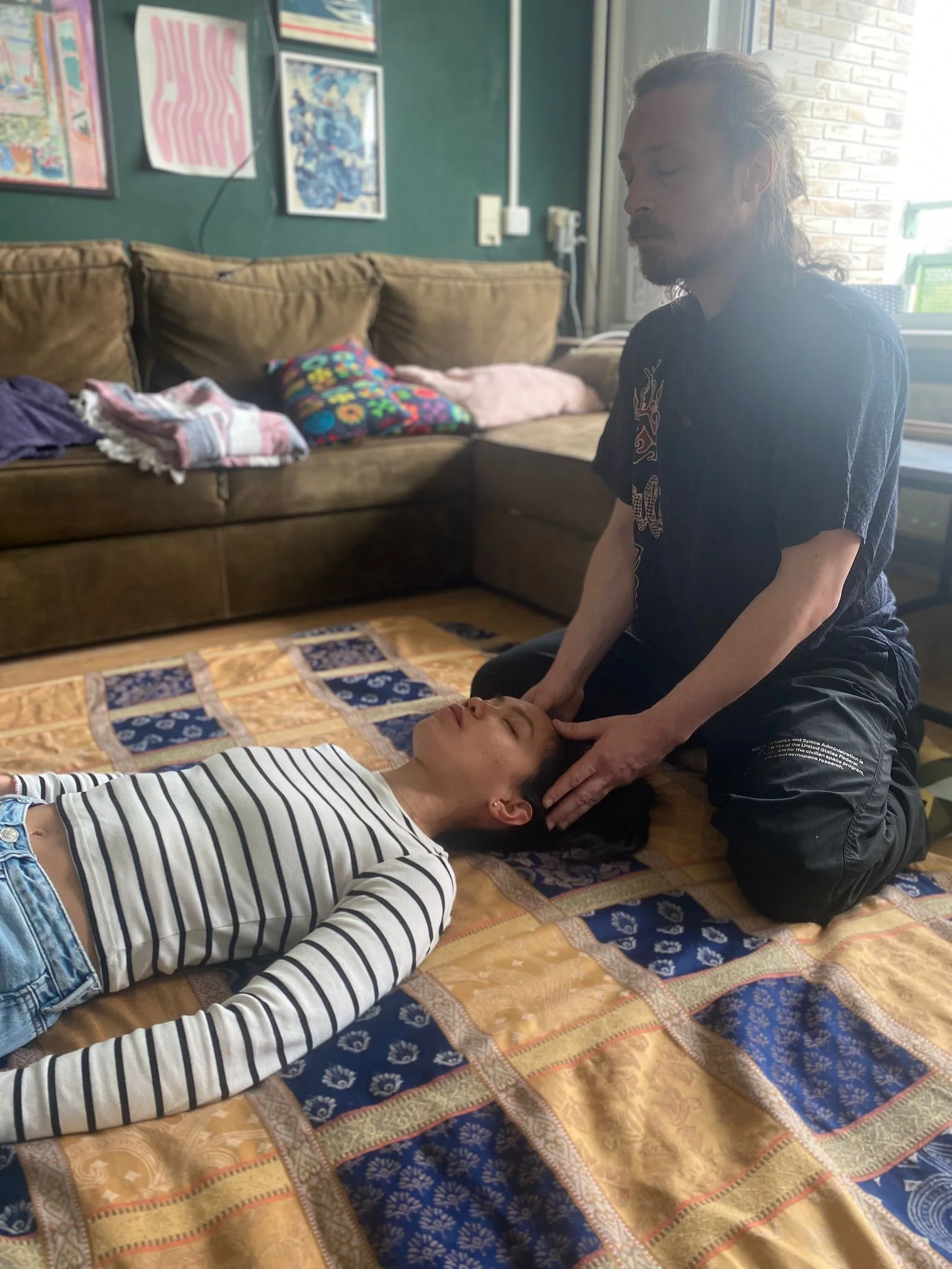 Een vrouw krijgt een hoofdmassage of shiatsu behandeling van een man, terwijl ze op de grond ligt.