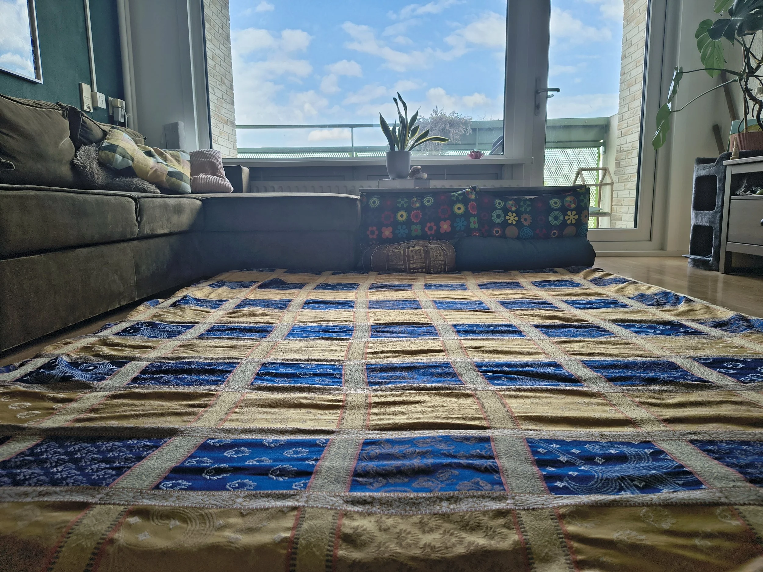 Een woonkamer met een bank, thee/koffietafel met planten, een groot raam met uitzicht op de blauwe lucht en een balkon. Japanse futon en een gezellige sfeer.