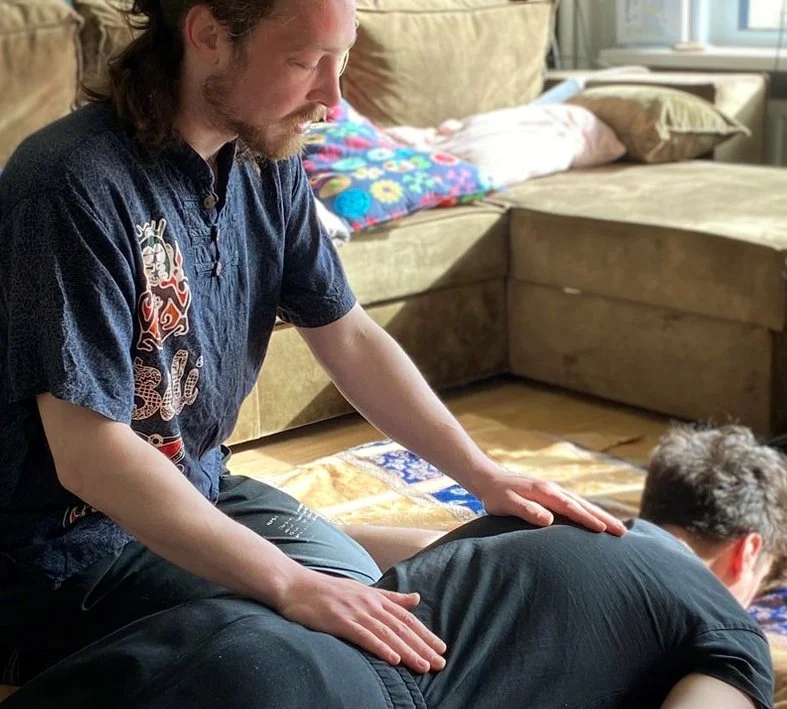 Man geeft een rugmassage aan een persoon die op de grond ligt in een woonkamer.