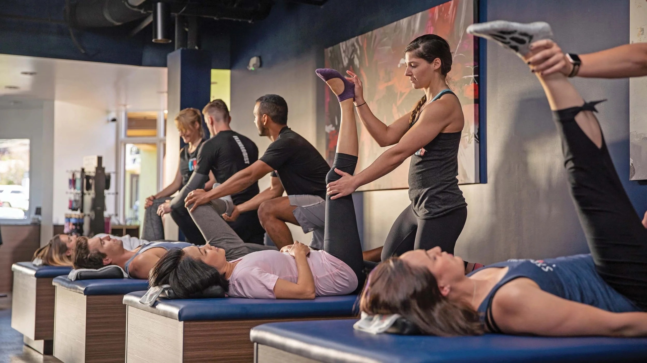 People lying on beds receiving physical therapy, with therapists stretching their legs in a gym or therapy center.