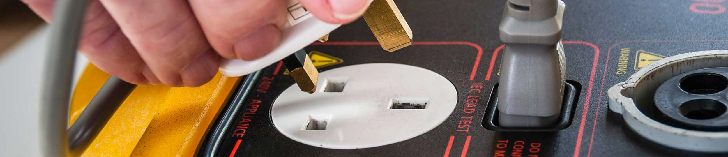 Close-up of a hand plugging a white electrical extension cord into a power outlet on a portable industrial power generator.