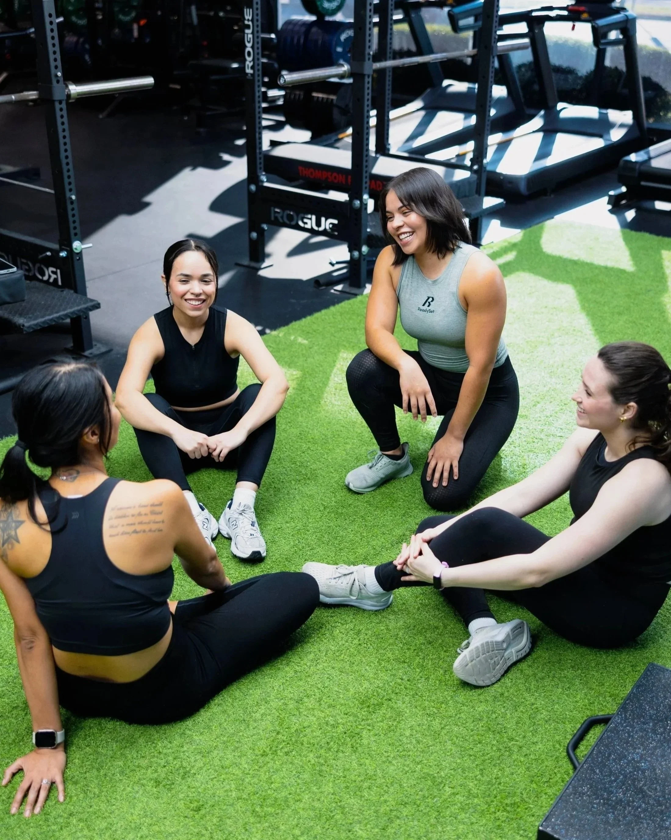 Women engaging in a group fitness class or workout session on green artificial turf at a gym or fitness center.
